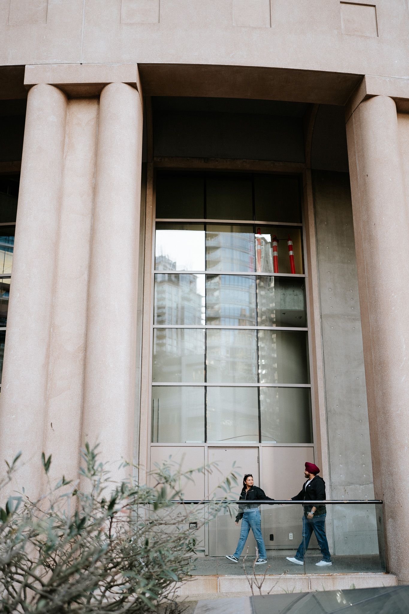 People walking past concrete columns and windows of a modern institutional building on an overcast day.