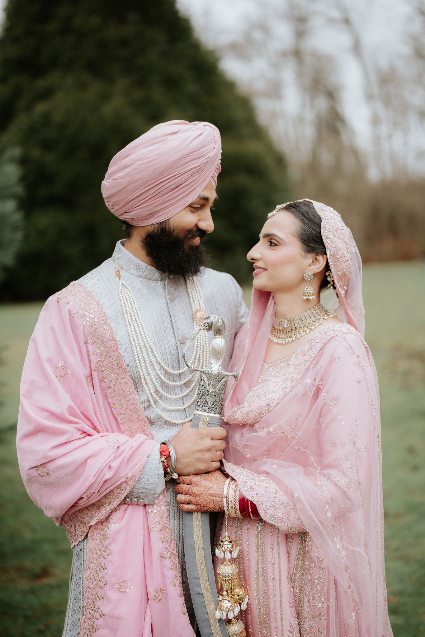 A couple in matching pink traditional Punjabi wedding attire share an intimate moment outdoors.