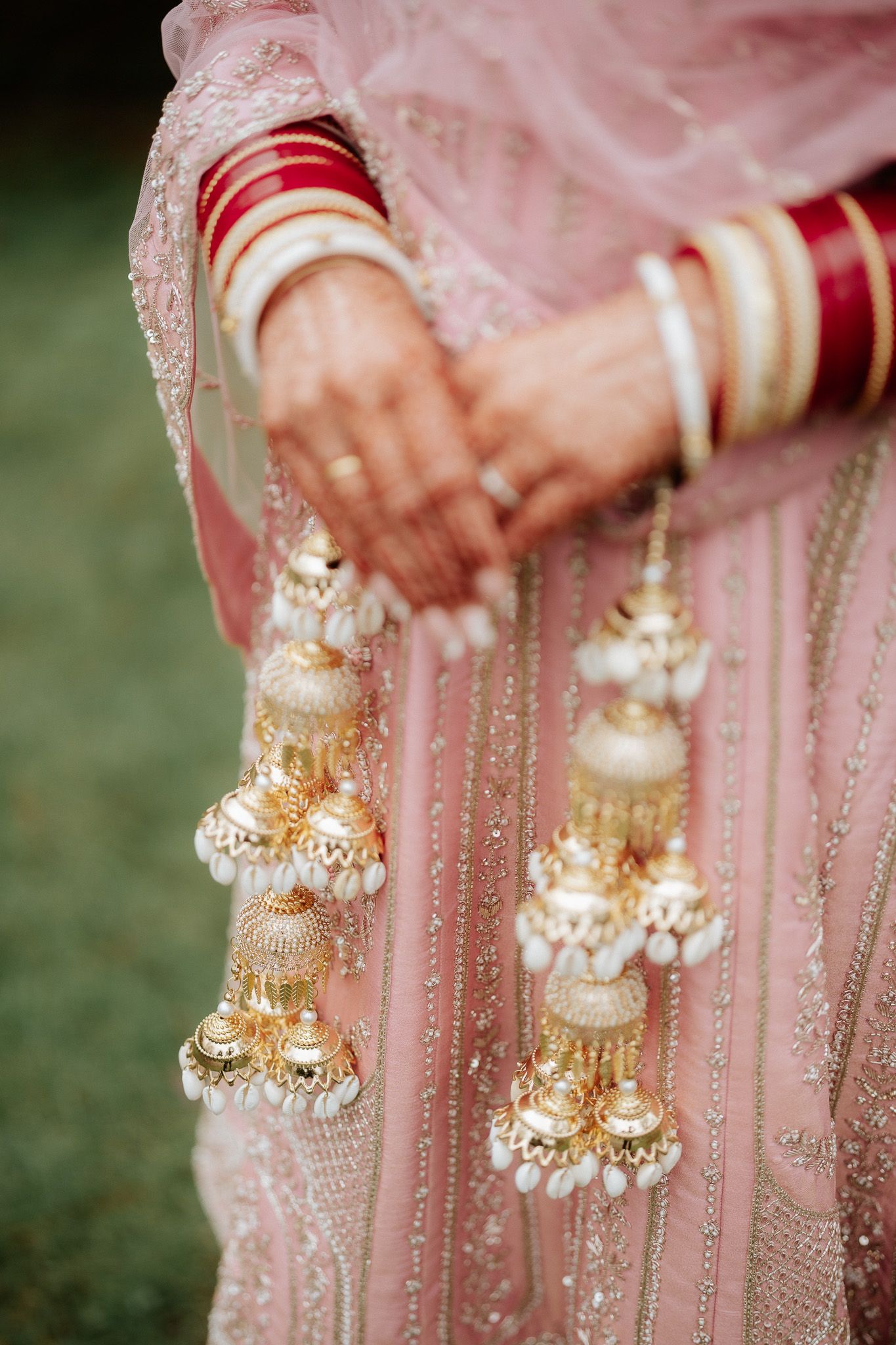 Close-up details of traditional Indian bridal jewelry with gold and pearl embellishments on pink fabric.
