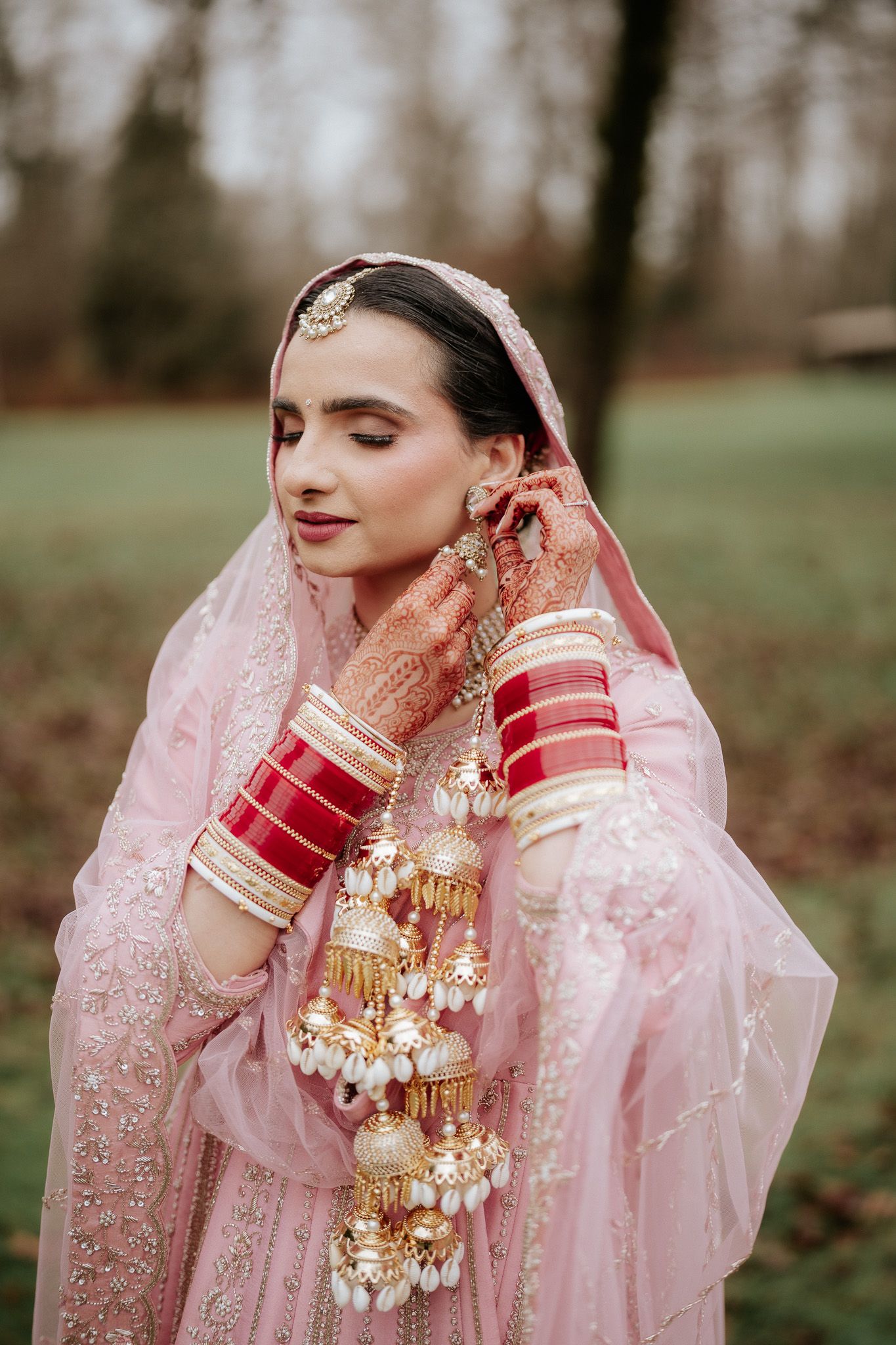 Close-up details of traditional Indian bridal jewelry and pink attire with intricate embellishments and henna-adorned hands.
