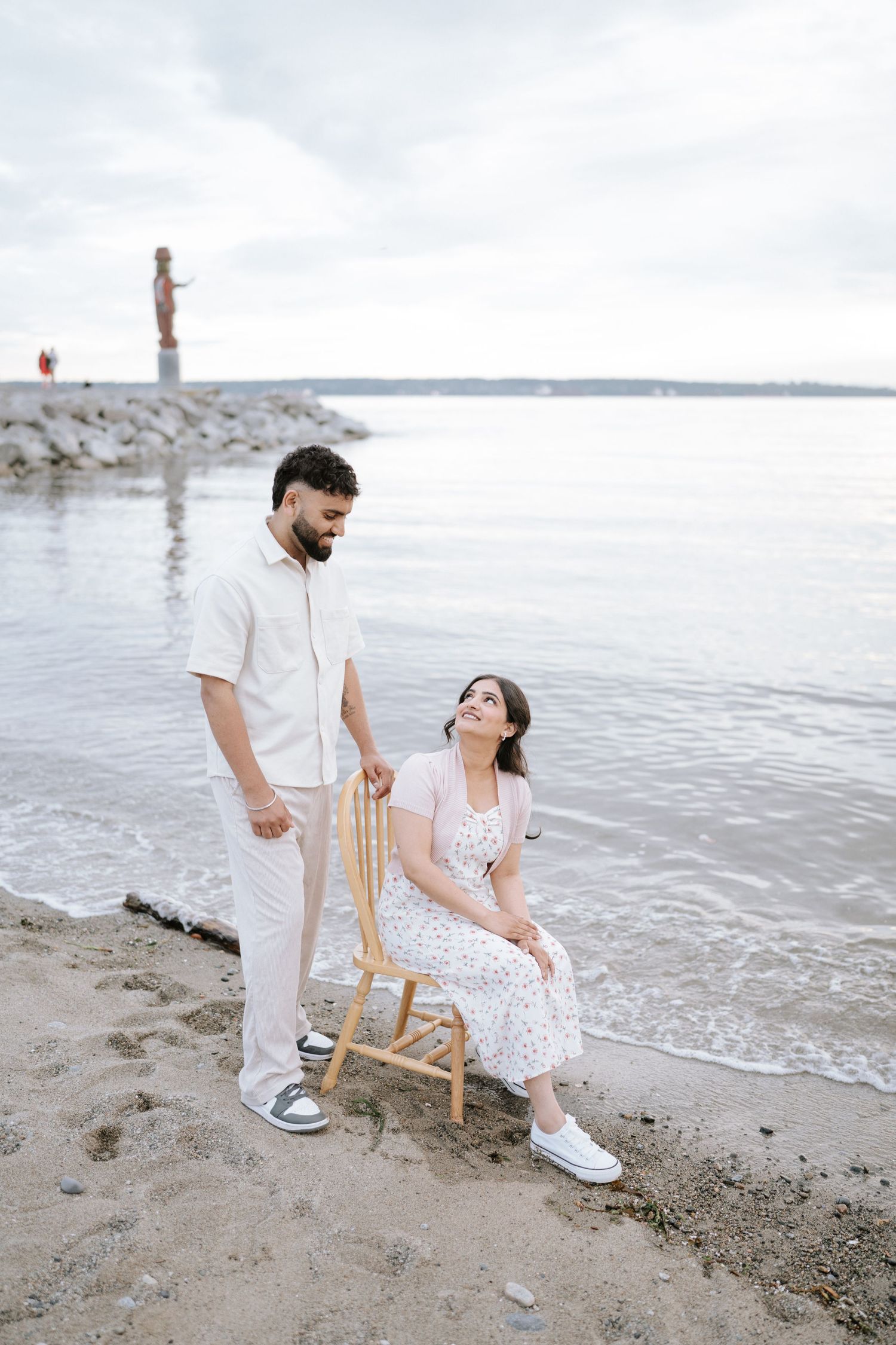 A romantic couple sits on a beach chair together near the water's edge.