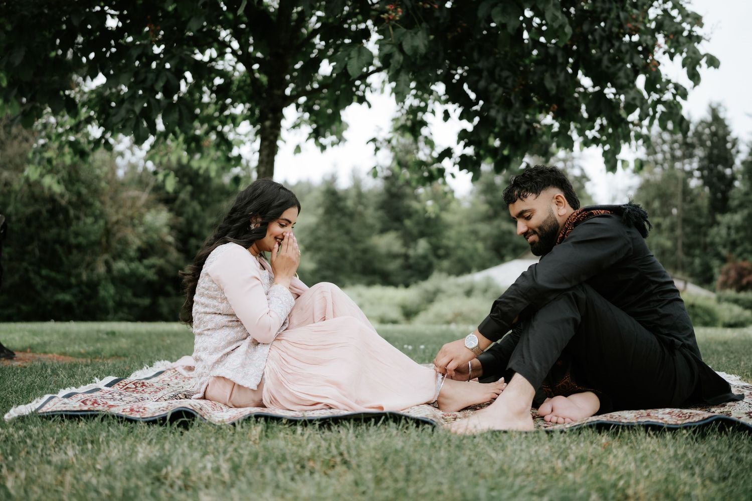 Two people enjoy a romantic afternoon on a blanket in a lush green park.