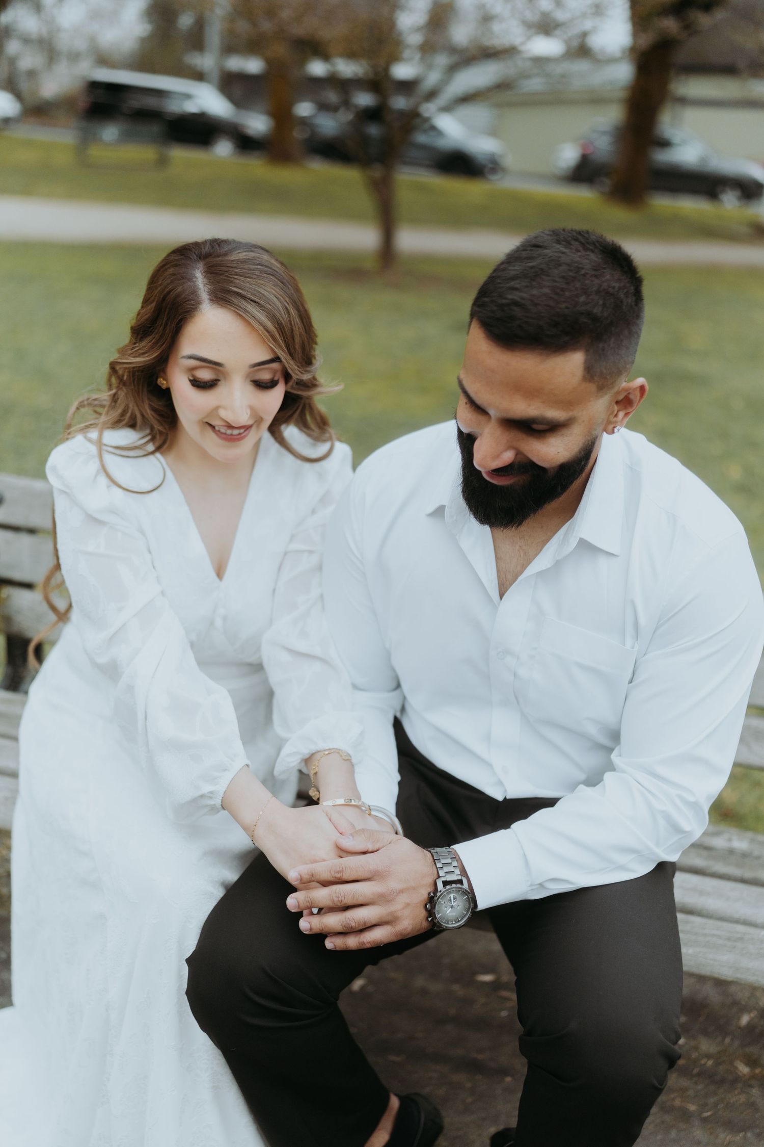 A couple in white shirts shares an intimate moment while sitting on a wooden bench outdoors.