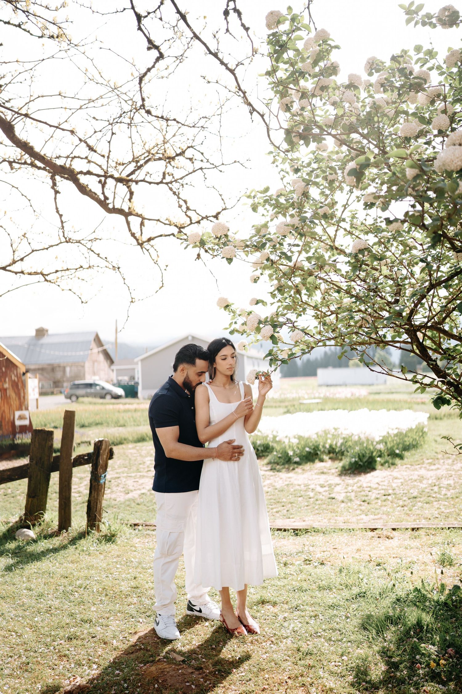 A couple dances together under blooming spring trees in a rustic outdoor setting during a sunny afternoon.