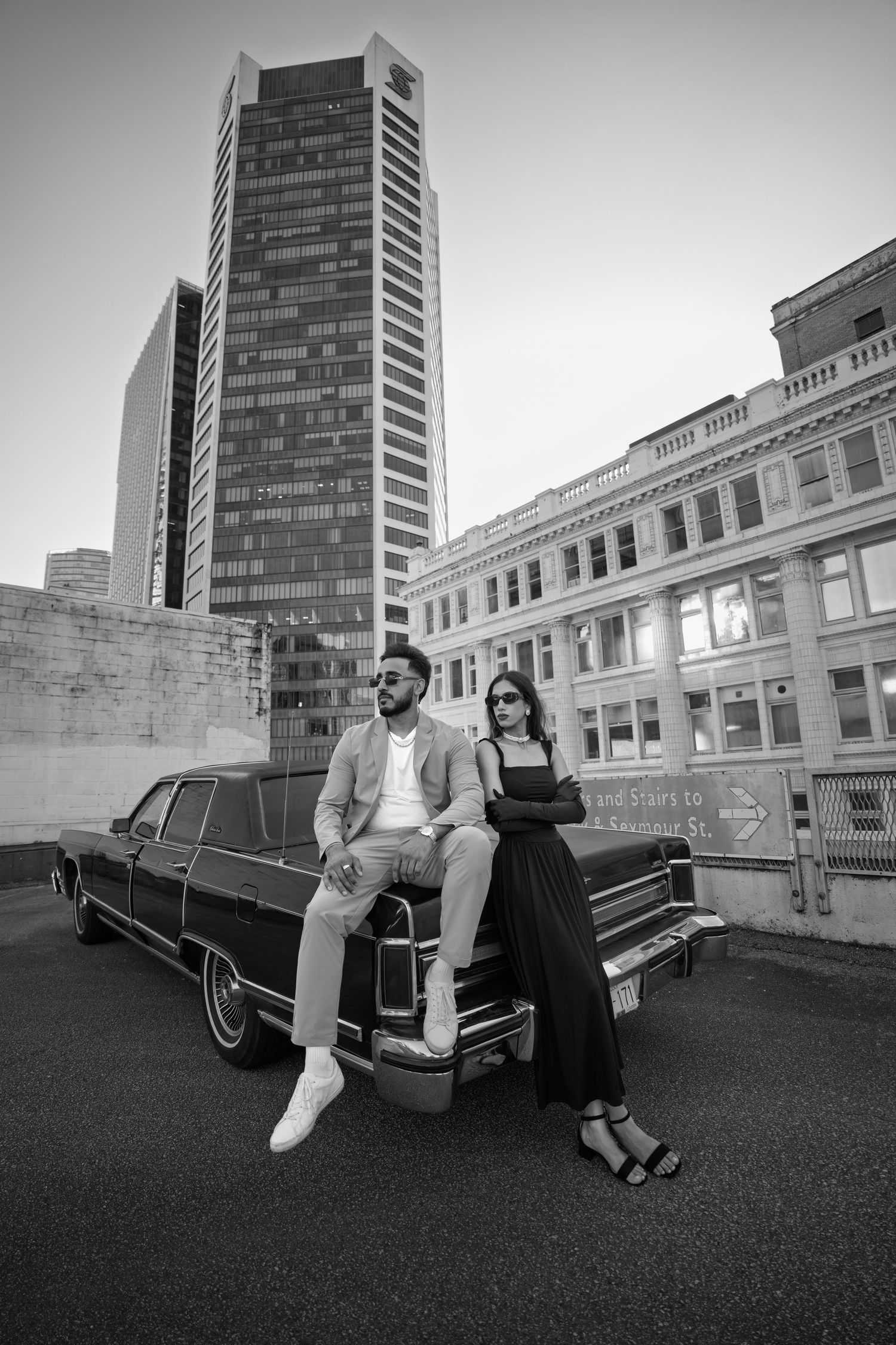Black and white photo series of a couple posing next to a vintage car on a rooftop with urban buildings in background.