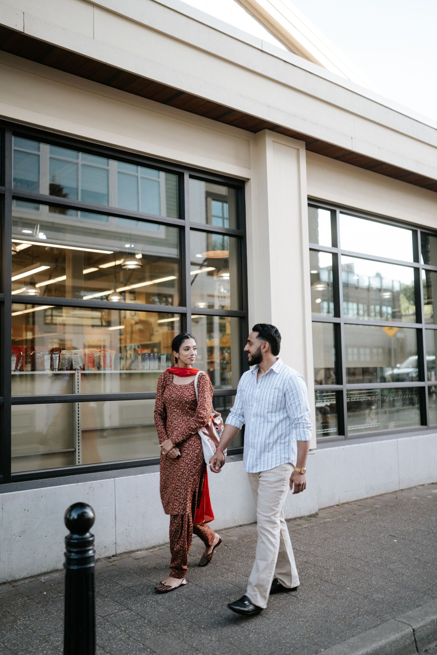 Two people walking and conversing outside a modern building with large glass windows.