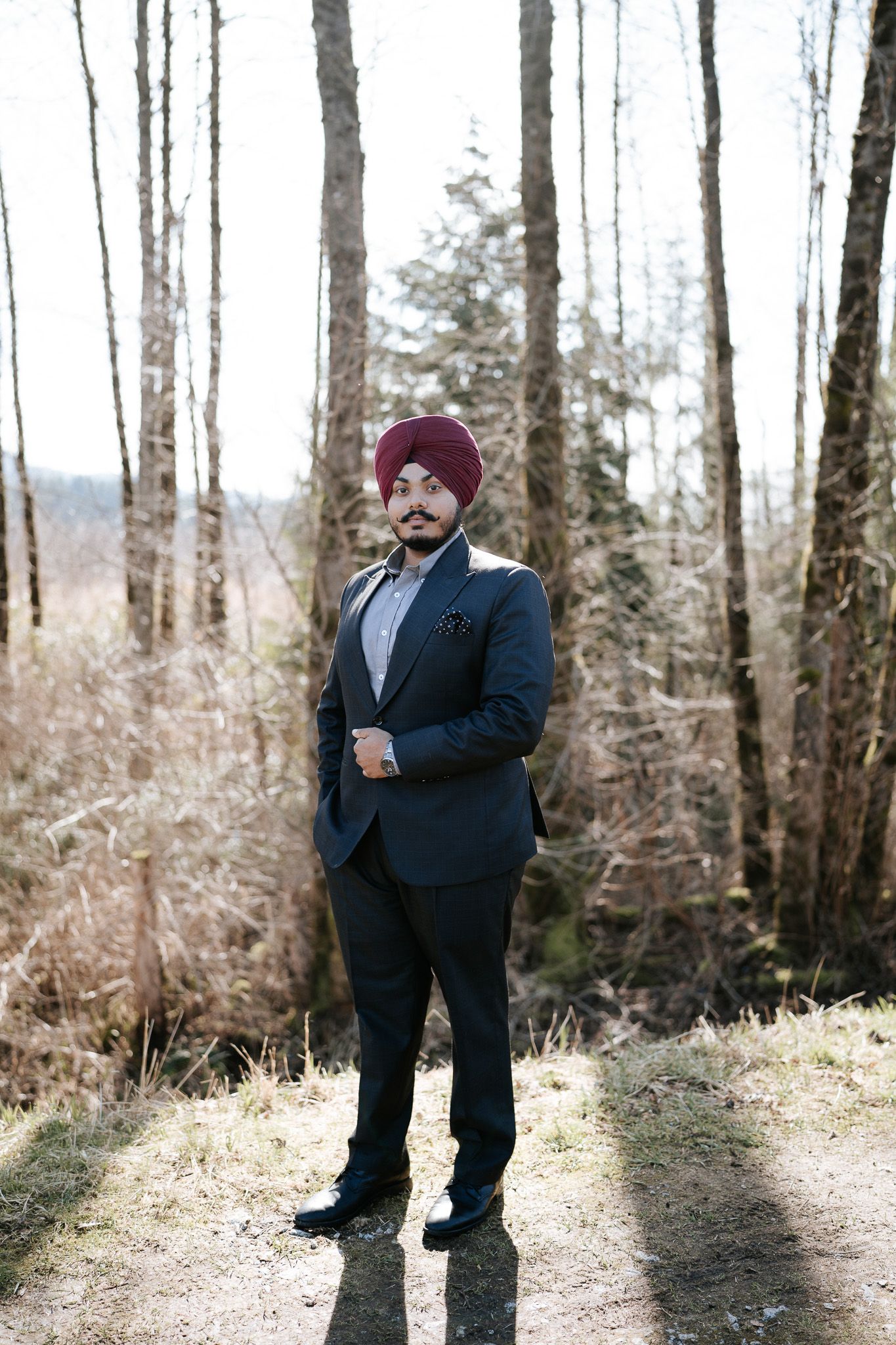 A group of people in formal attire stand in a wooded area during a winter photo session.