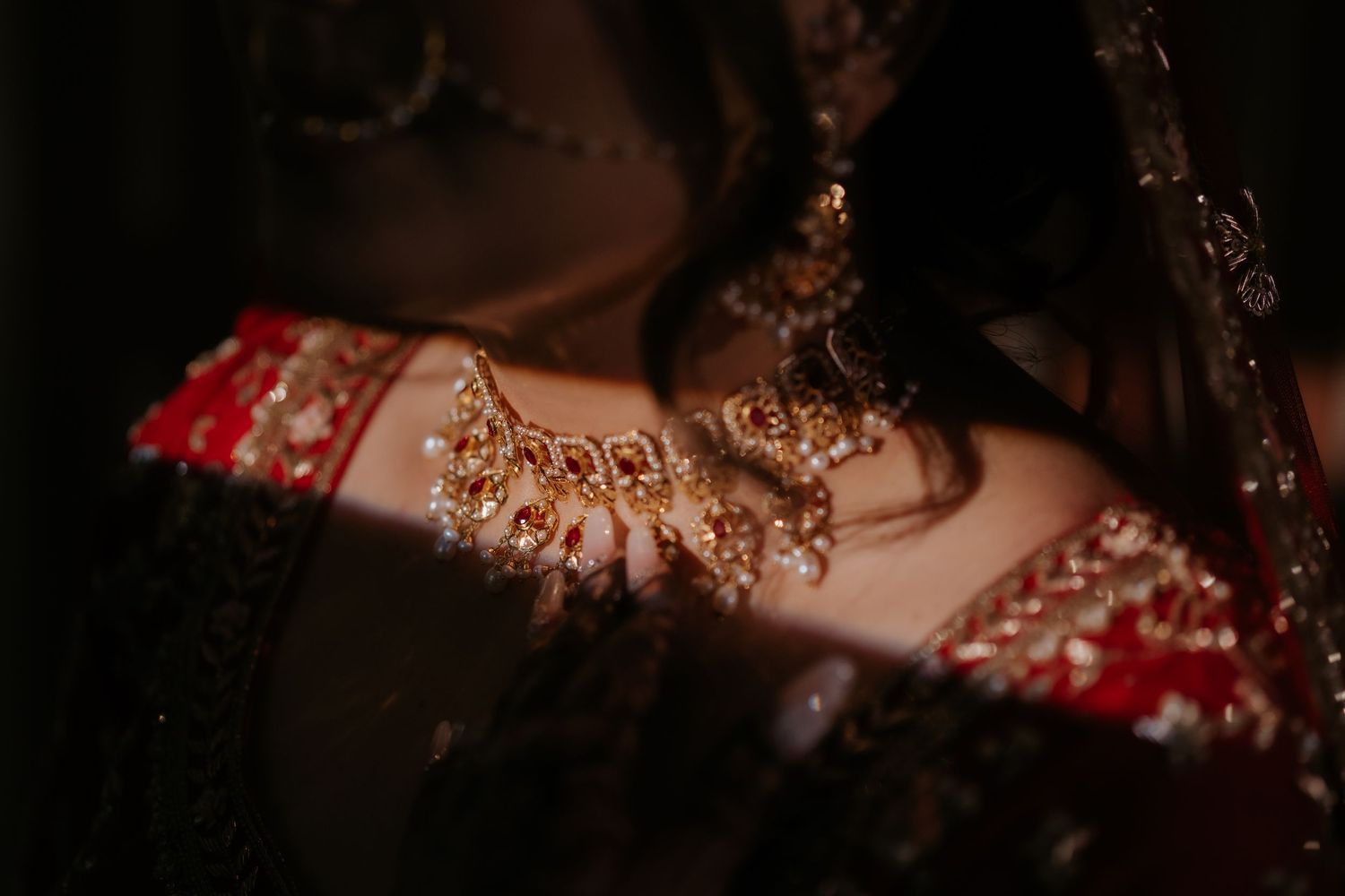 Close-up of a bride wearing ornate gold and ruby bridal jewelry with intricate embroidery on a red lehenga.