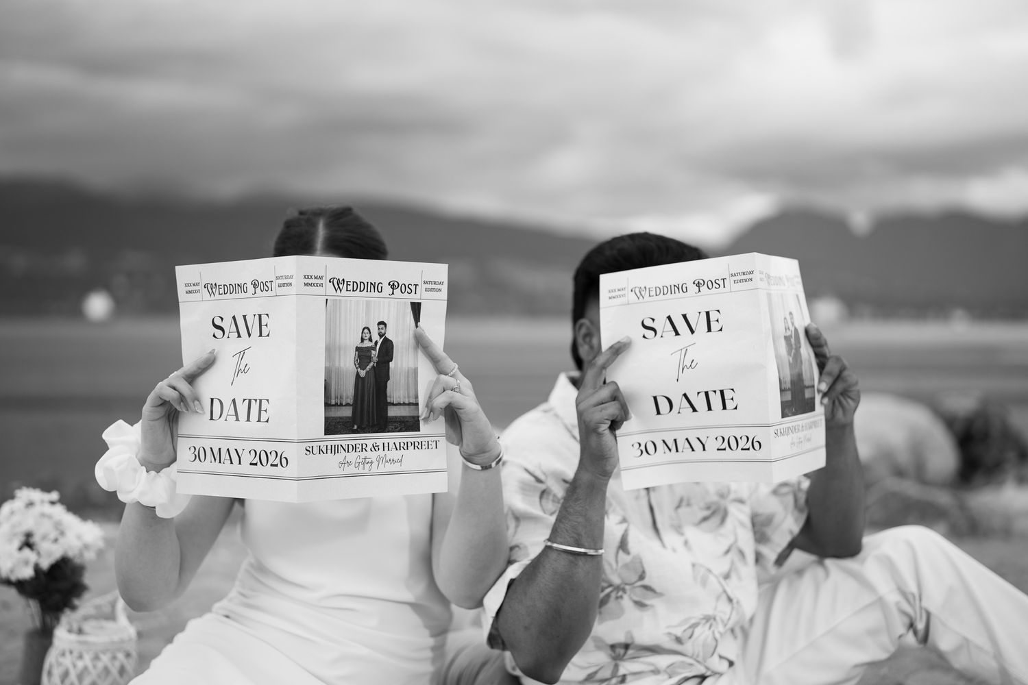 Couple holding Save the Date wedding newspapers outdoors in black and white photo, date reads 30 May 2026.