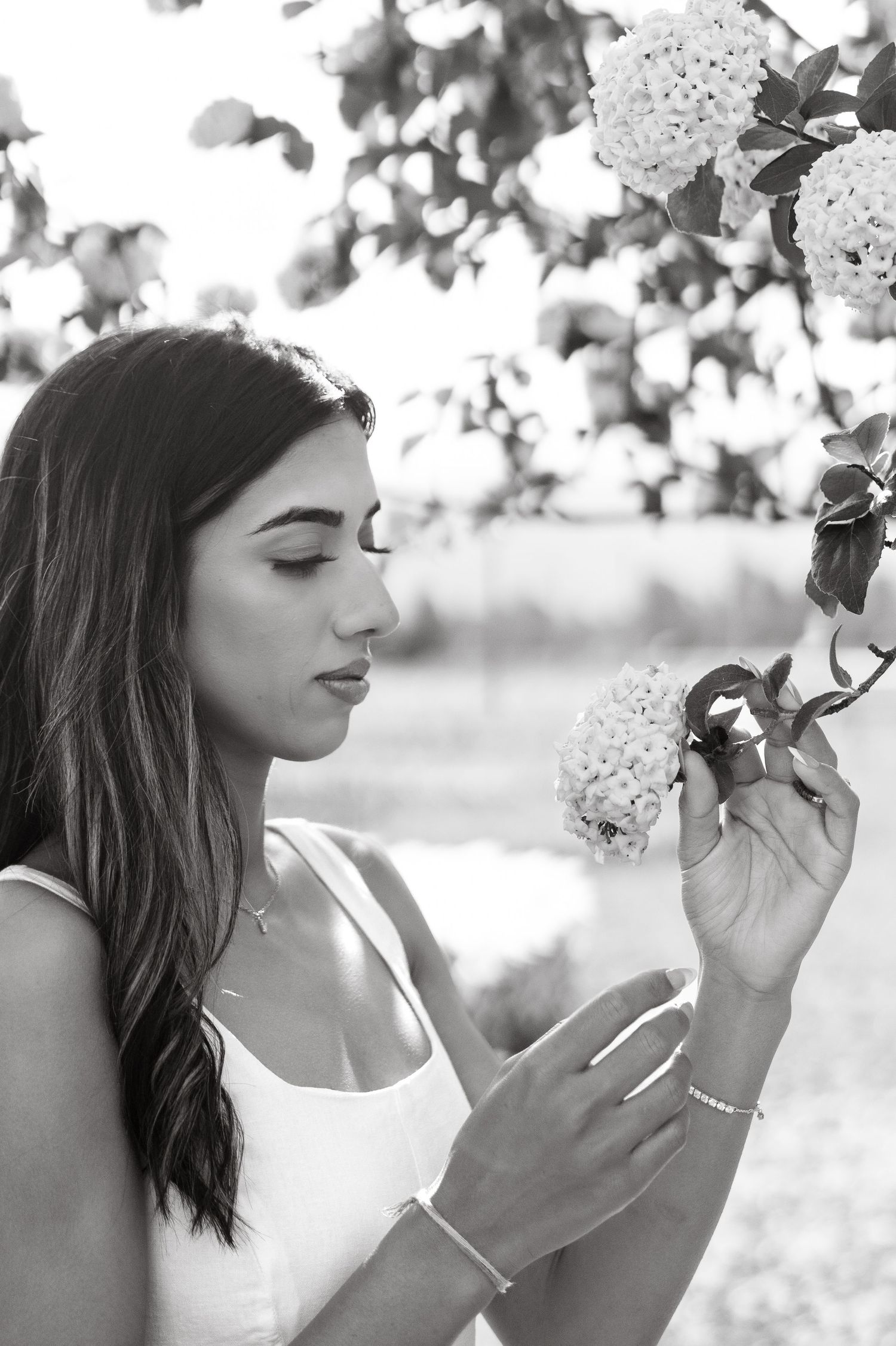 Black and white photo series showing someone in a white top smelling flowers in a dreamy outdoor setting.