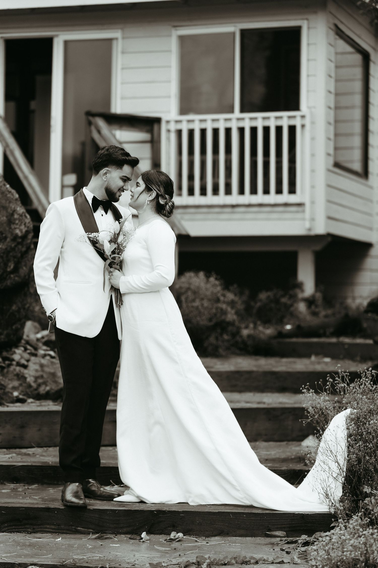 Black and white wedding photo with flowing white dress train against residential backdrop.