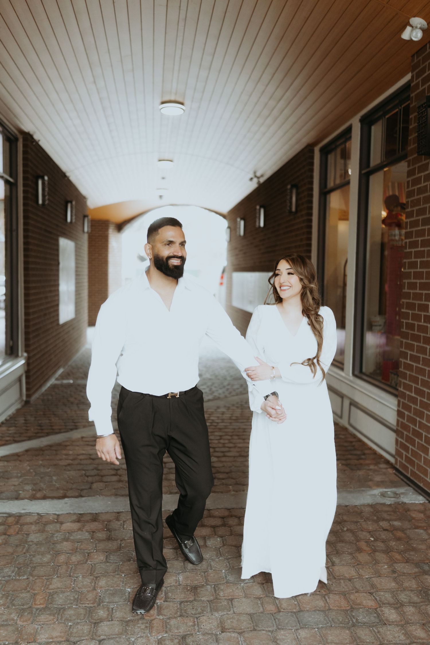 Dancing couple in formal wear creates joyful moments in brick-lined corridor.