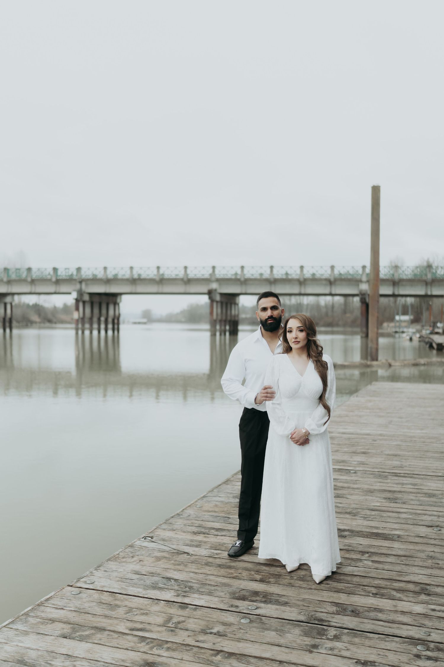 A romantic photoshoot on a wooden pier with a couple in white and black attire.