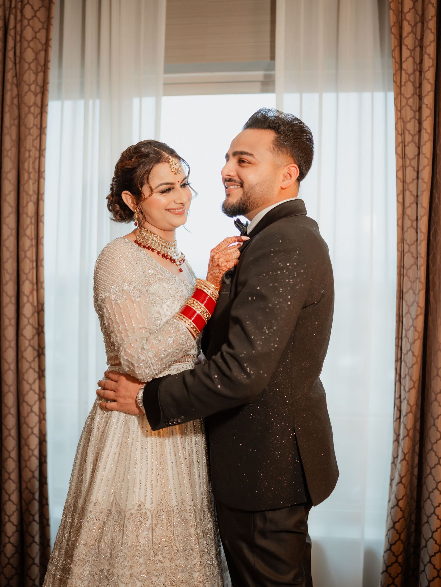 A tender moment between a couple in traditional wedding attire with decorative curtains in background.