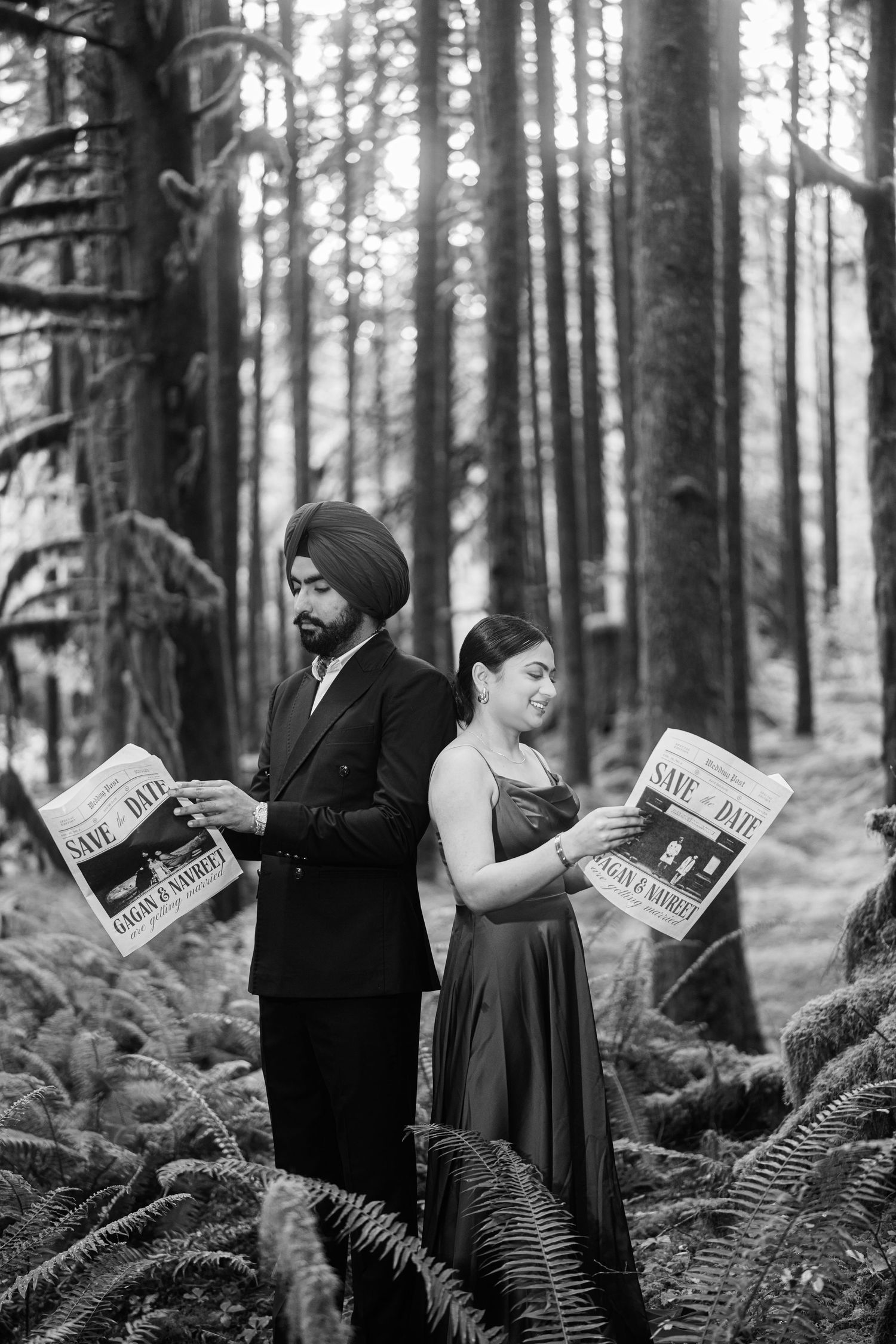 A couple in formal attire poses with newspapers in a misty forest setting among tall trees and ferns.