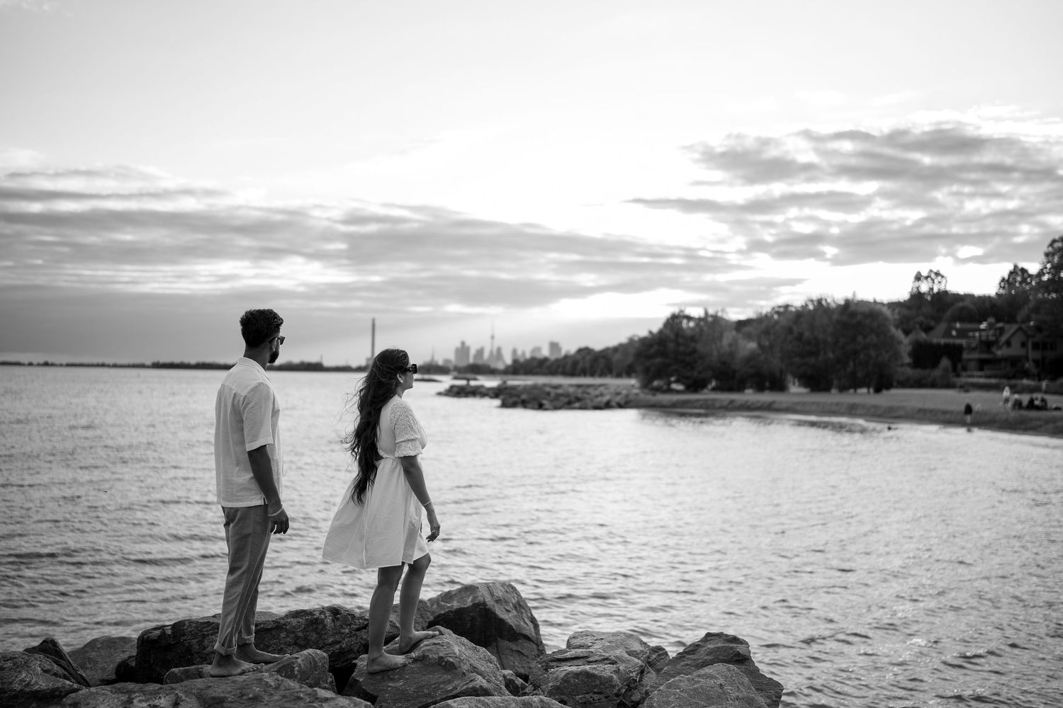 Silhouetted couple watching sunset over water from rocky shoreline.