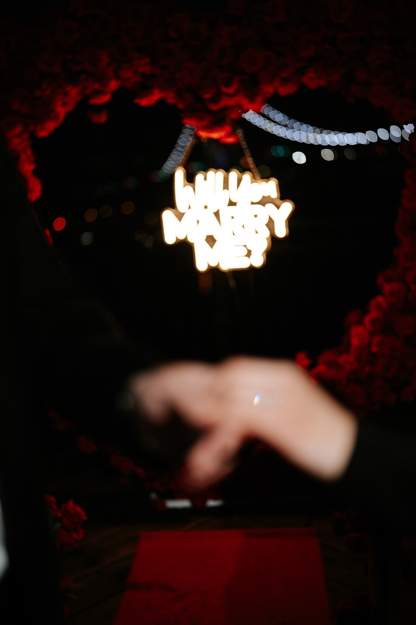 Glowing neon text signs in red and white illuminate a dark nighttime scene with blurred elements.