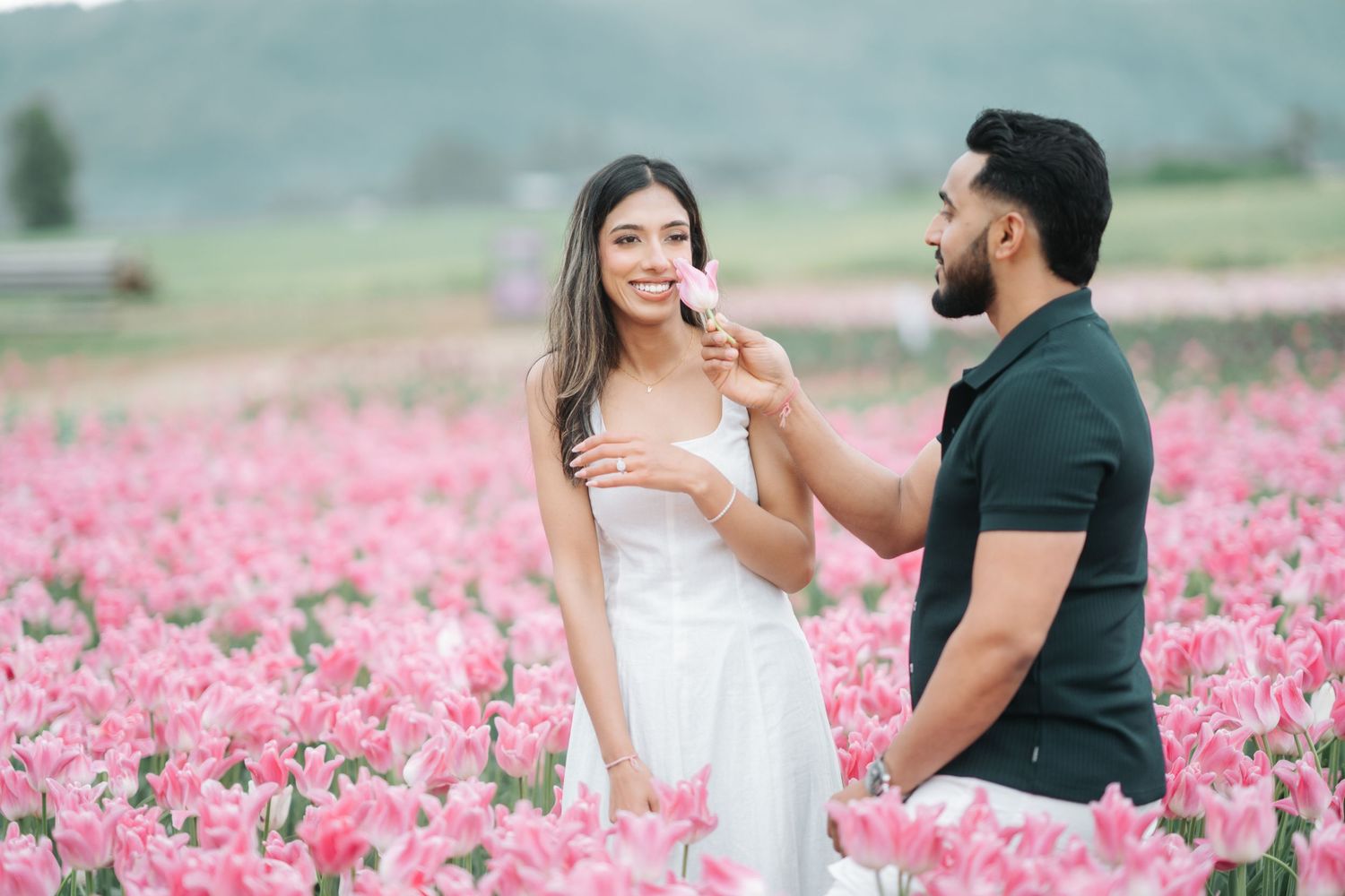 A couple shares a romantic moment in a vibrant pink tulip field on a misty spring day.