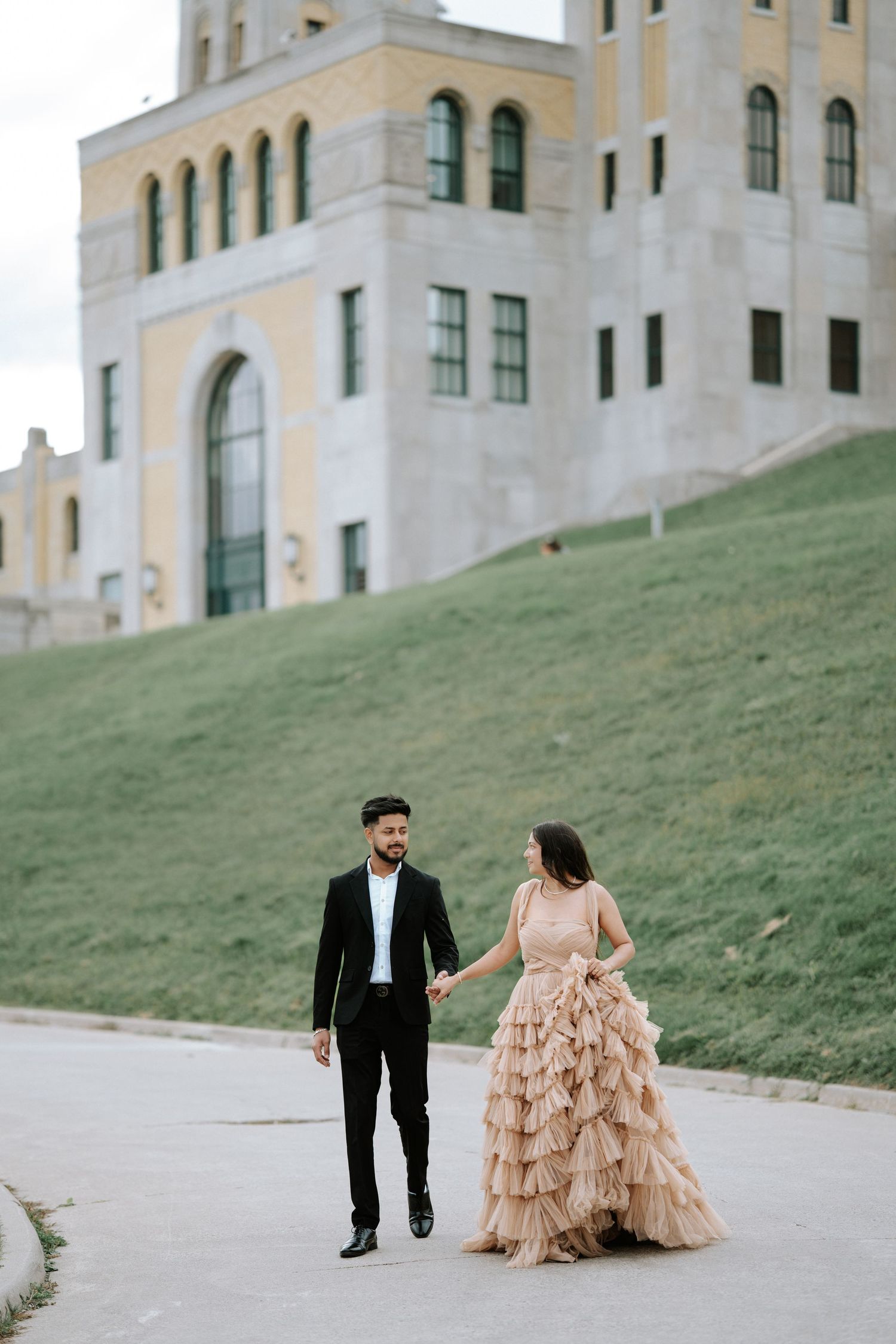 Couple in formal attire walking together outside modern architectural building.