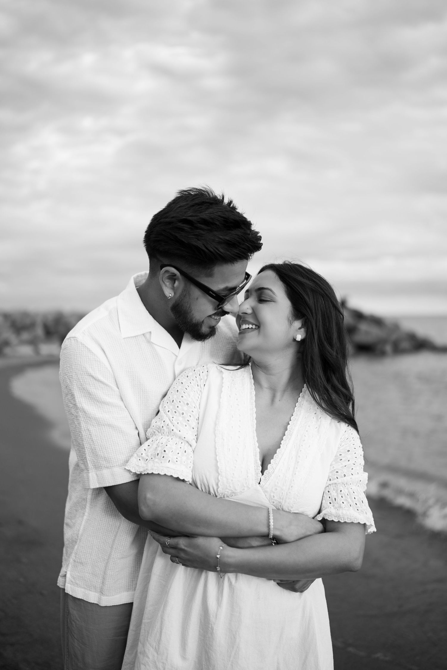 Intimate black and white portraits of couple sharing tender moments by the coast.