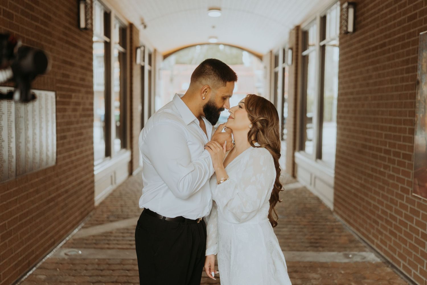 Series of romantic poses captured in a sunlit brick corridor with architectural details.