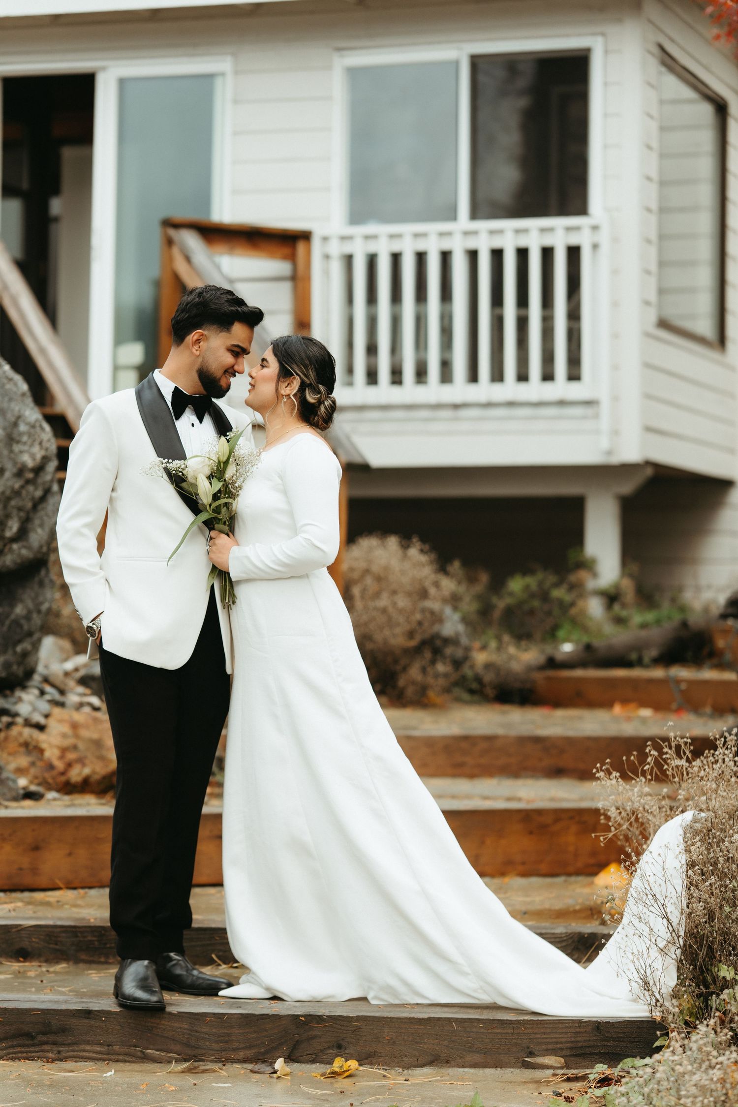 Romantic wedding couple shares intimate moments in a series of outdoor photos by a white house with a porch.