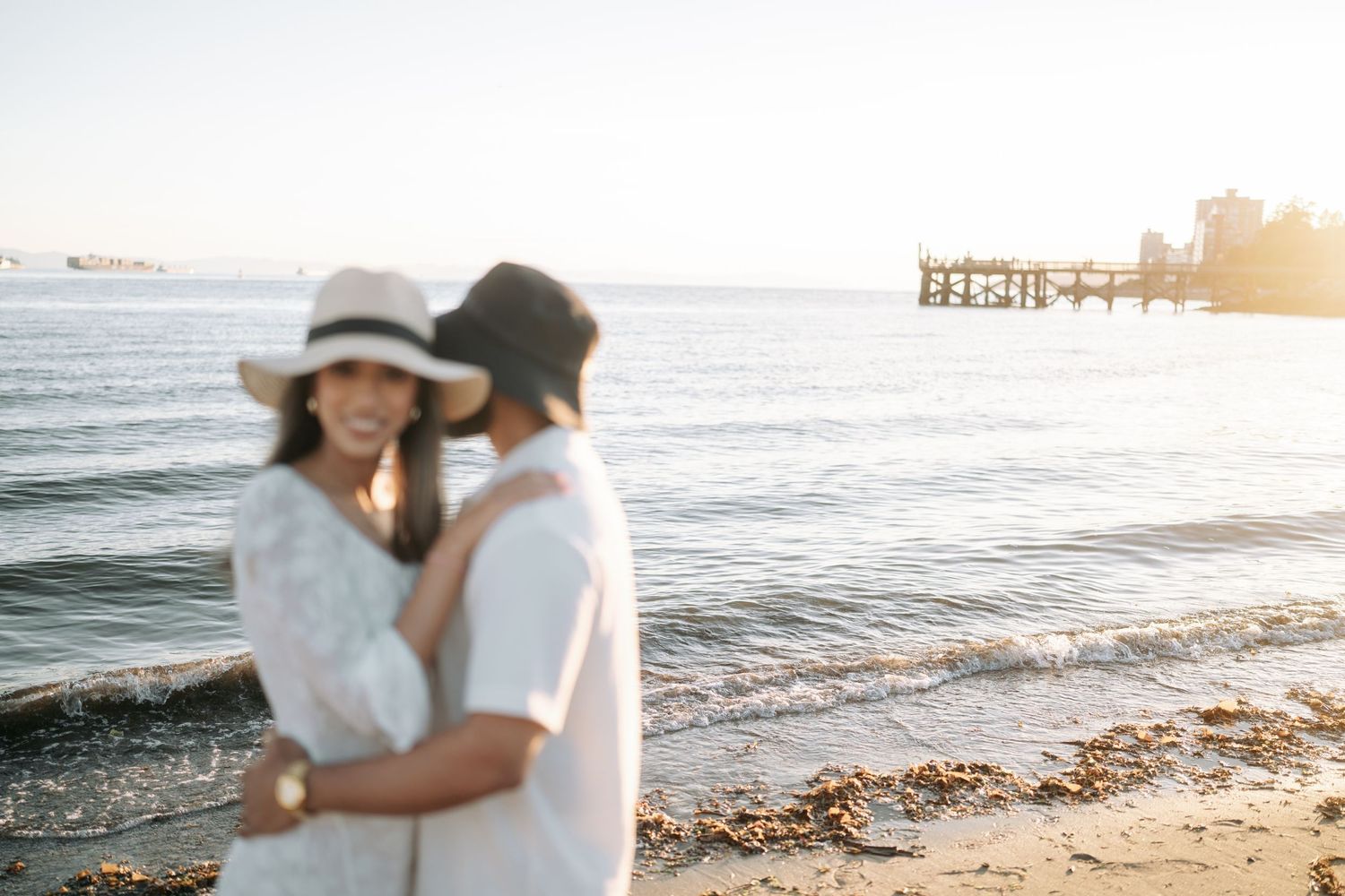 A romantic couple embraces on a sunny beach at sunset, creating a serene and intimate moment by the ocean.