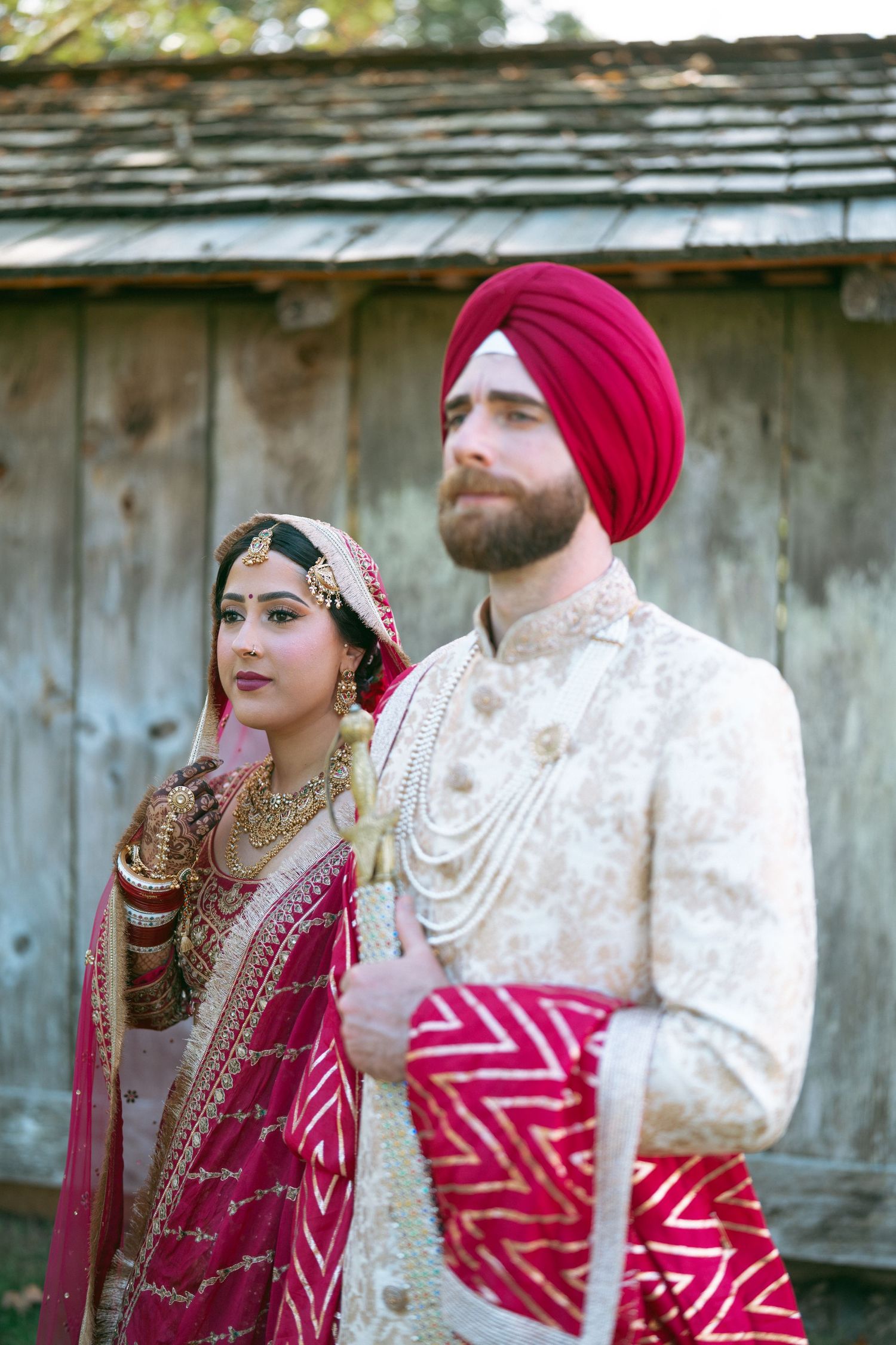 Sikh bride and groom in traditional wedding attire, bride in red lehenga, groom in cream sherwani and red turban.