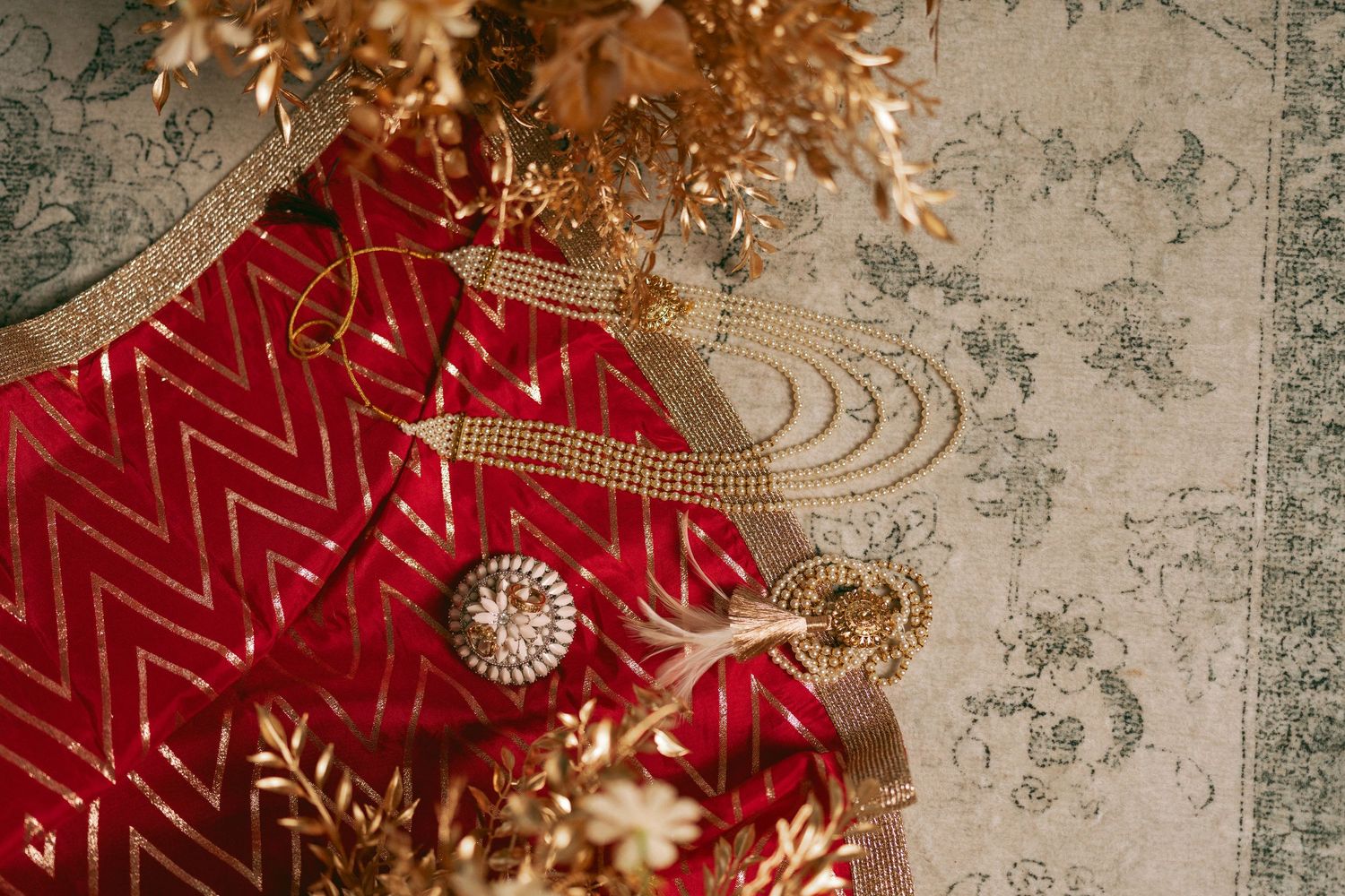 Red chevron silk lehenga with gold embroidery and ornate bridal jewelry displayed on decorative carpet.