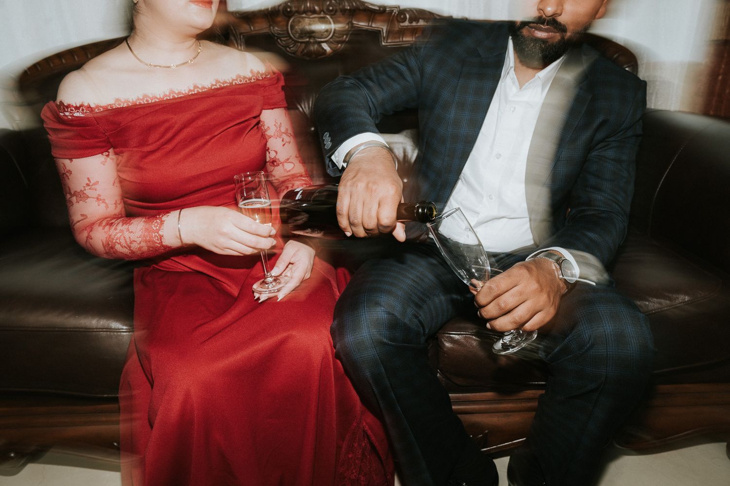 Couple in formal attire sharing wine while seated together on a leather sofa.