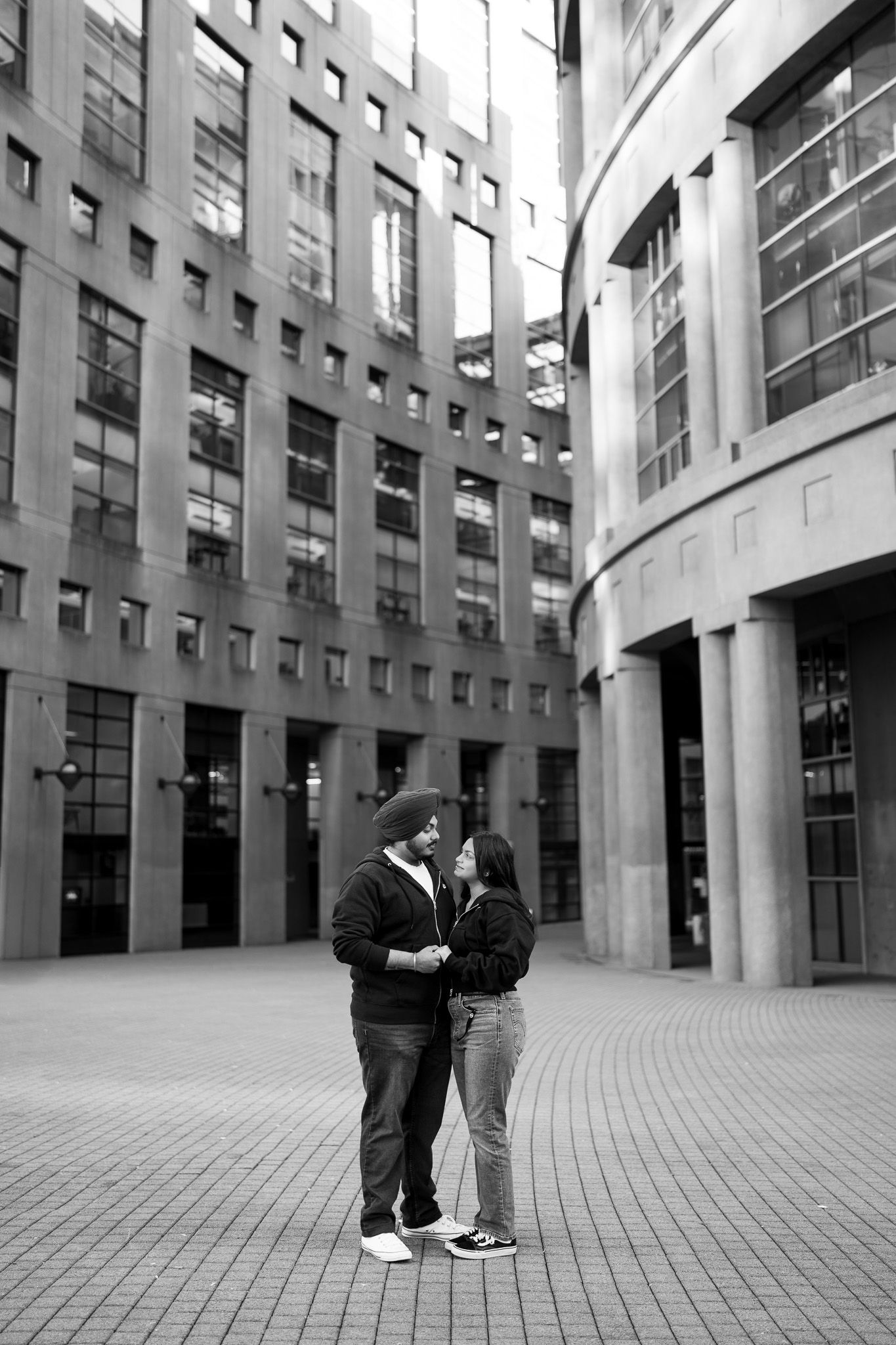 A couple shares an intimate moment in a modern architectural courtyard with tall columns and curved paving stones.