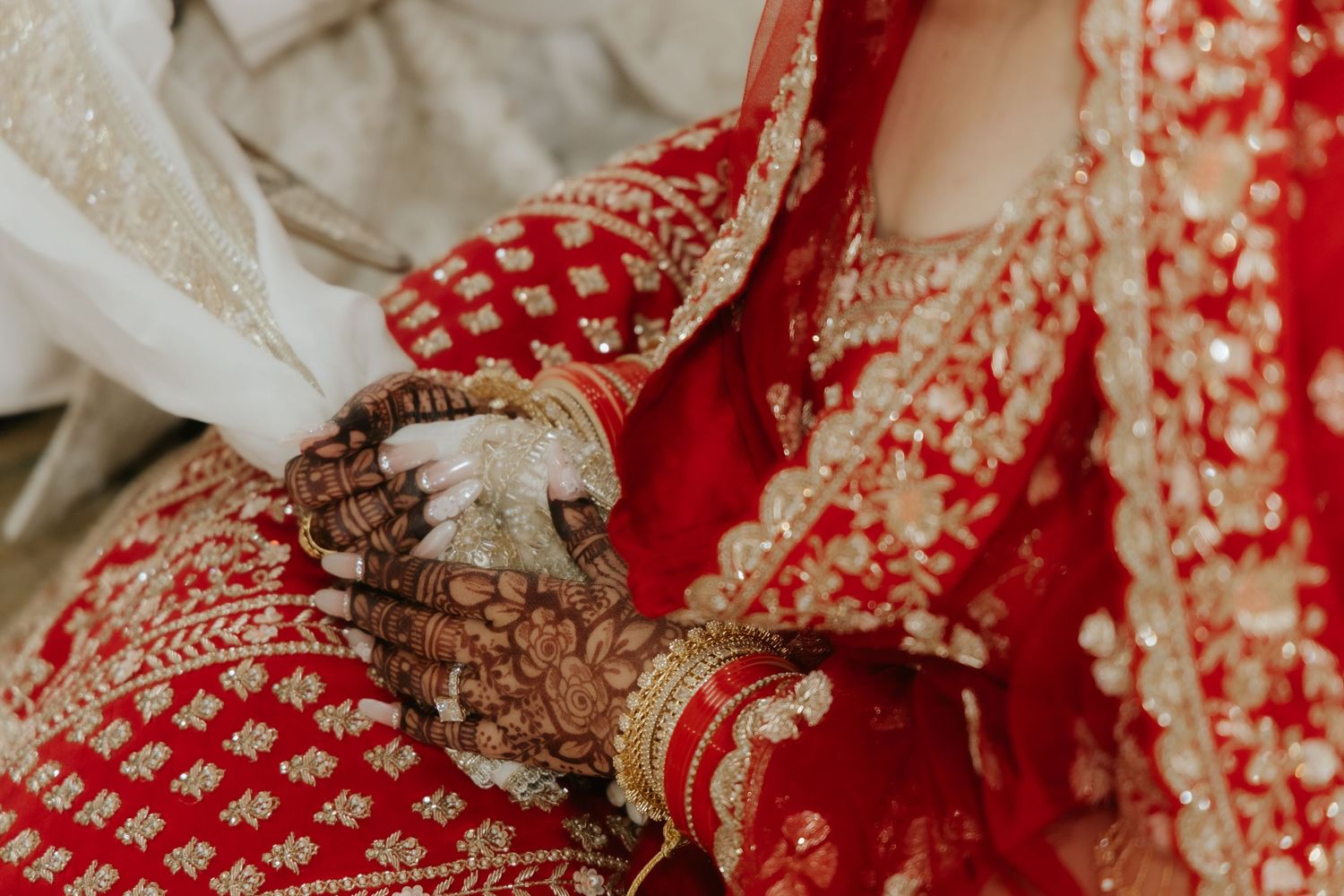 Bride in red bridal lehenga with intricate mehndi henna designs on hands at Indian wedding ceremony.