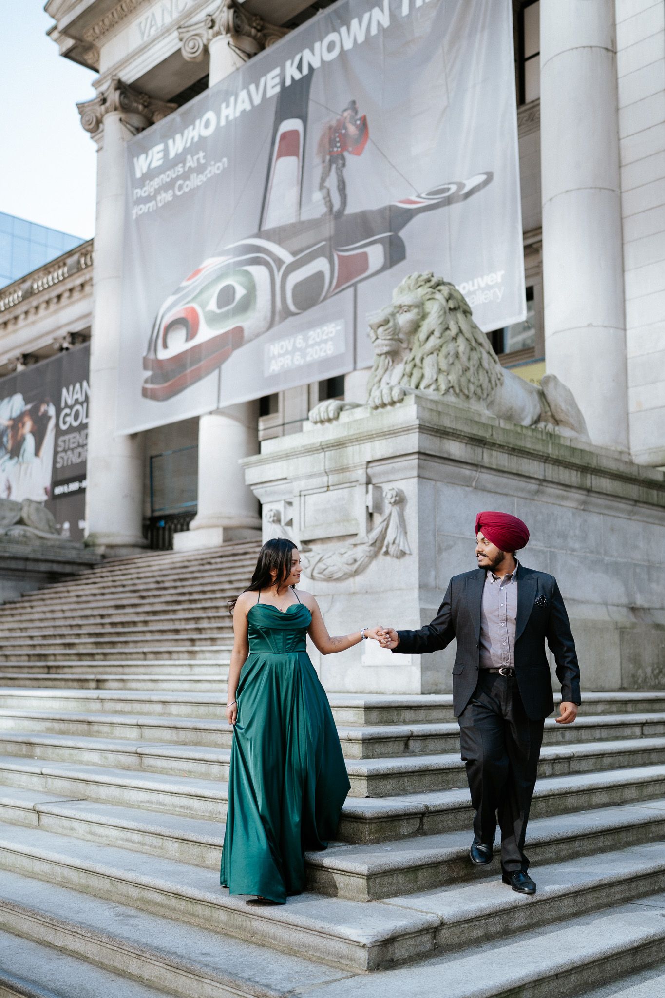A couple shares romantic moments on grand stone steps outside a building with classical columns and lion statues.