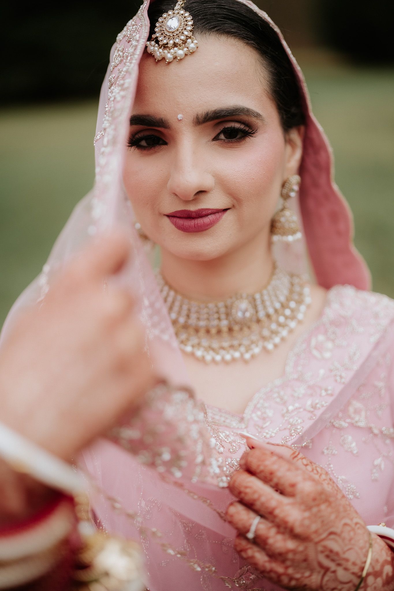 Traditional Indian bridal portrait series showing detailed pink outfit, jewelry, and mehndi in outdoor setting.