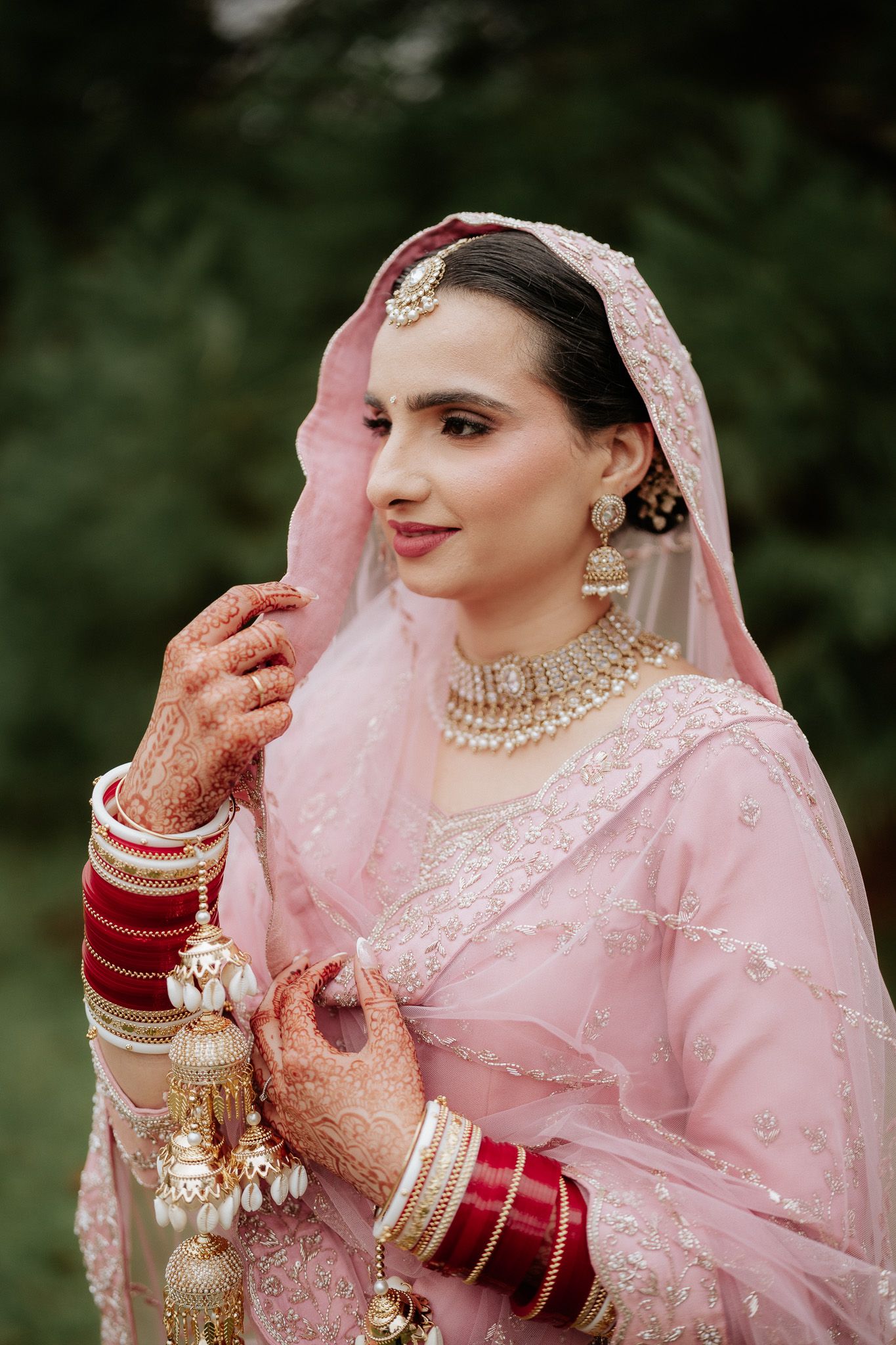 Traditional Indian bridal attire in soft pink with intricate gold embellishments and jewelry.