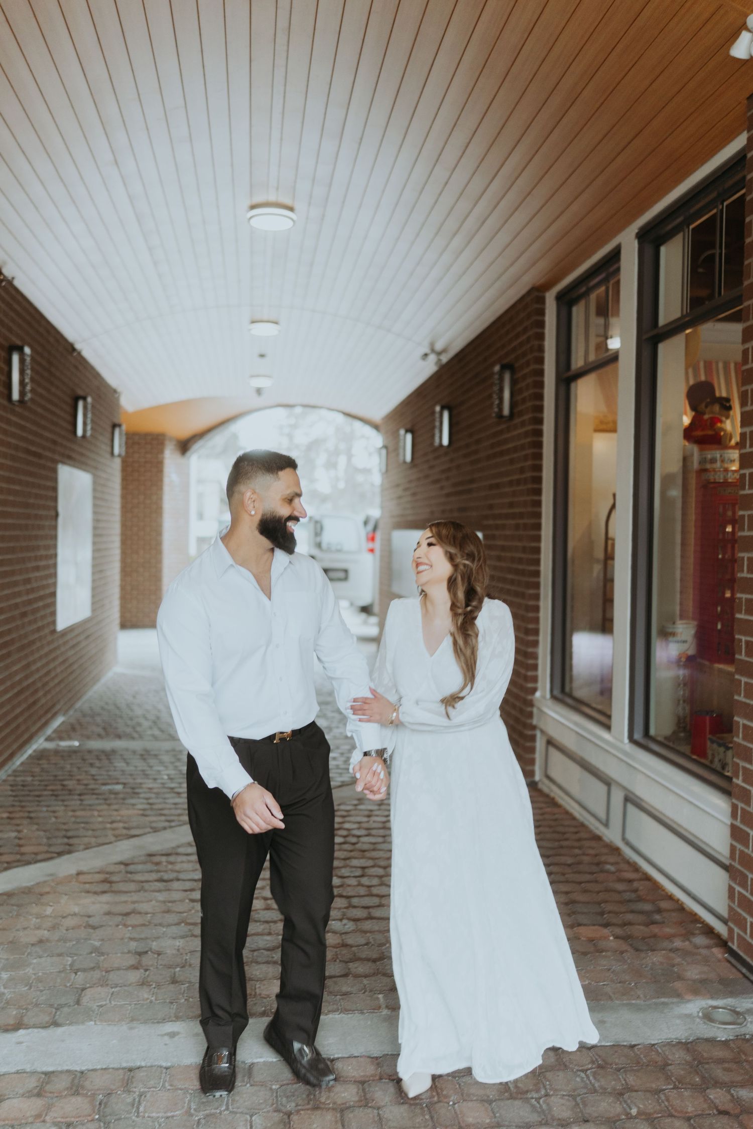 A couple shares an intimate moment in a brick-lined hallway with white paneled ceiling.