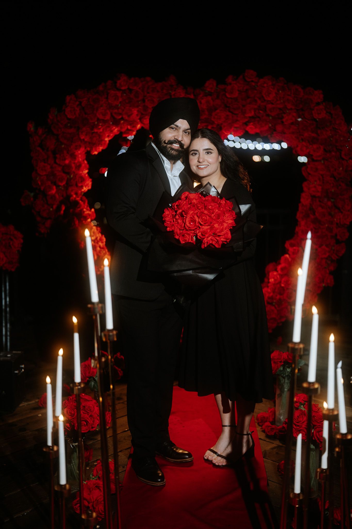 A romantic photoshoot scene with white candles and red floral decor against a dark backdrop.