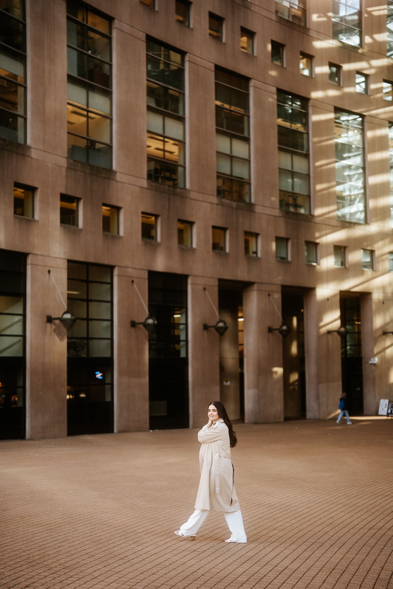 Figure in white clothing stands alone in front of a modern office building with tall windows.