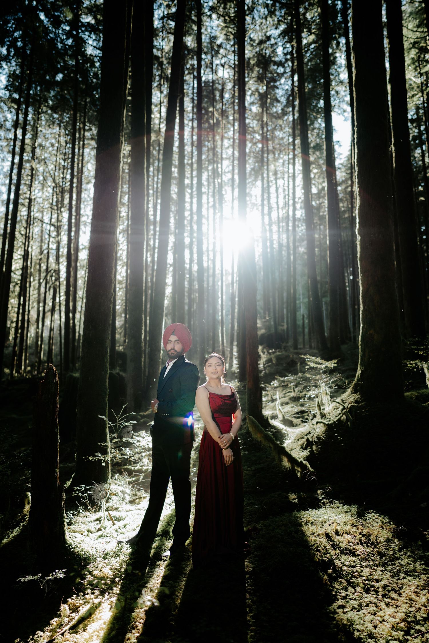 Dramatic forest photoshoot with sunlight streaming through tall trees creating ethereal lighting effects.