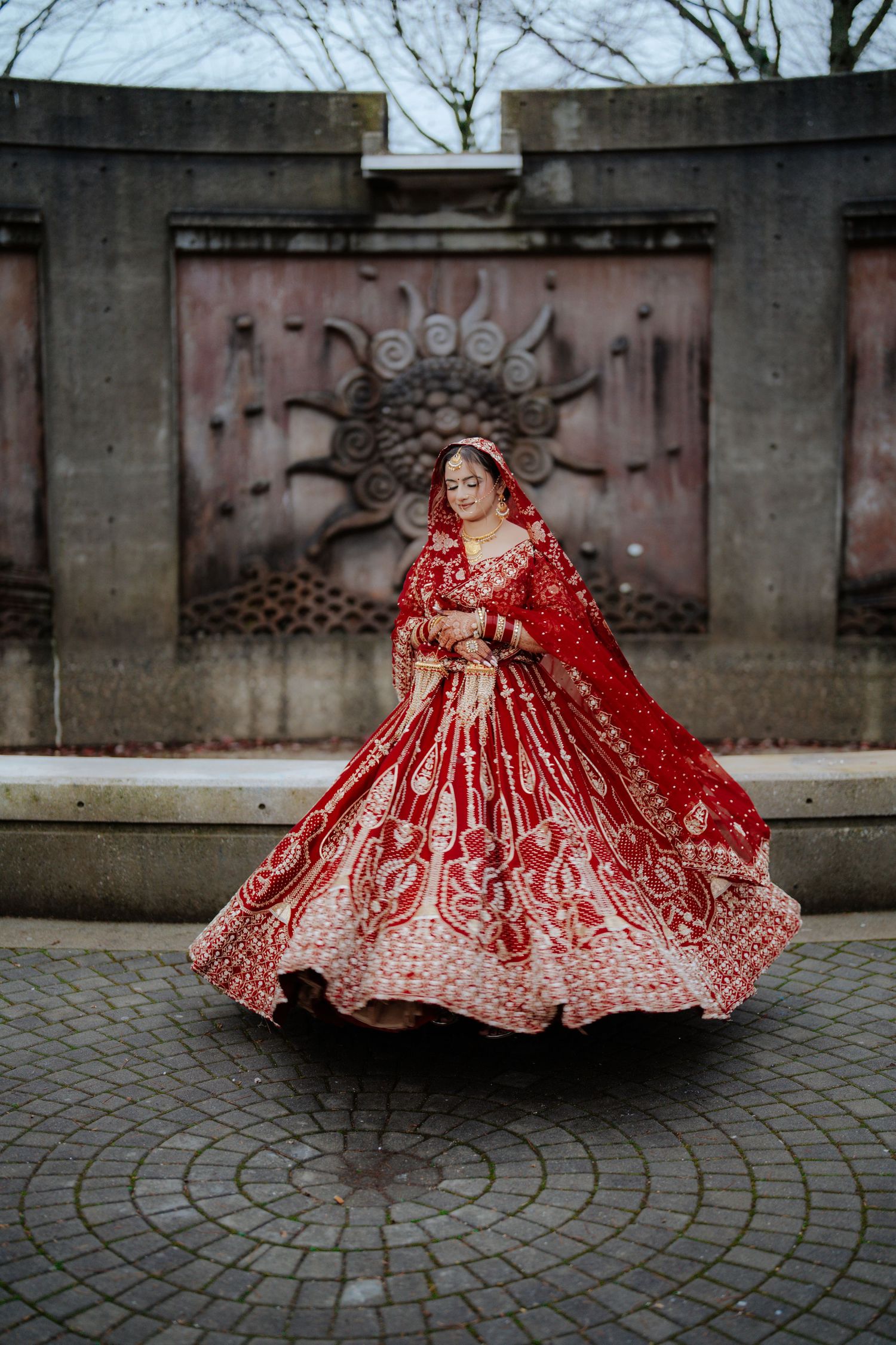 Artistic shots of red bridal lehenga flowing on circular cobblestone pattern.