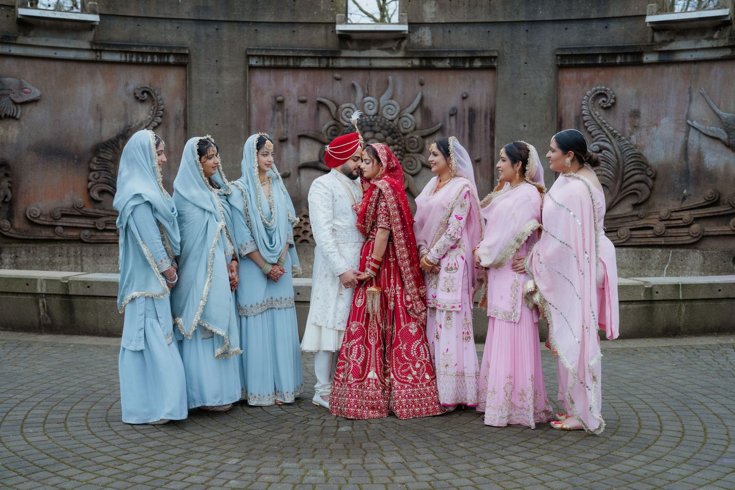 Wedding party poses outdoors with bridesmaids in pastel colors and couple in traditional red and white.