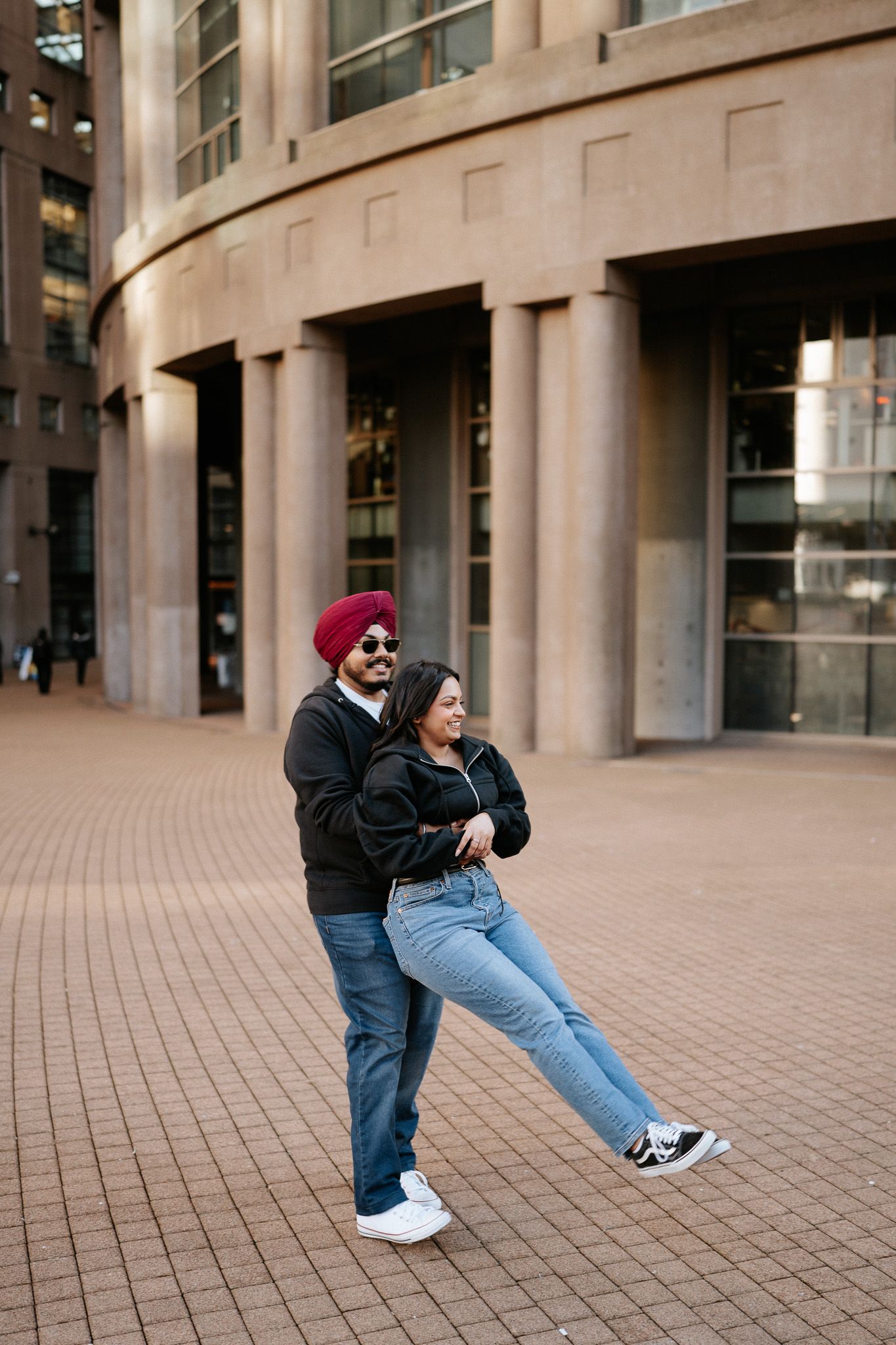 A sequence of four images showing a couple playfully leaning and posing against a modern building's exterior.