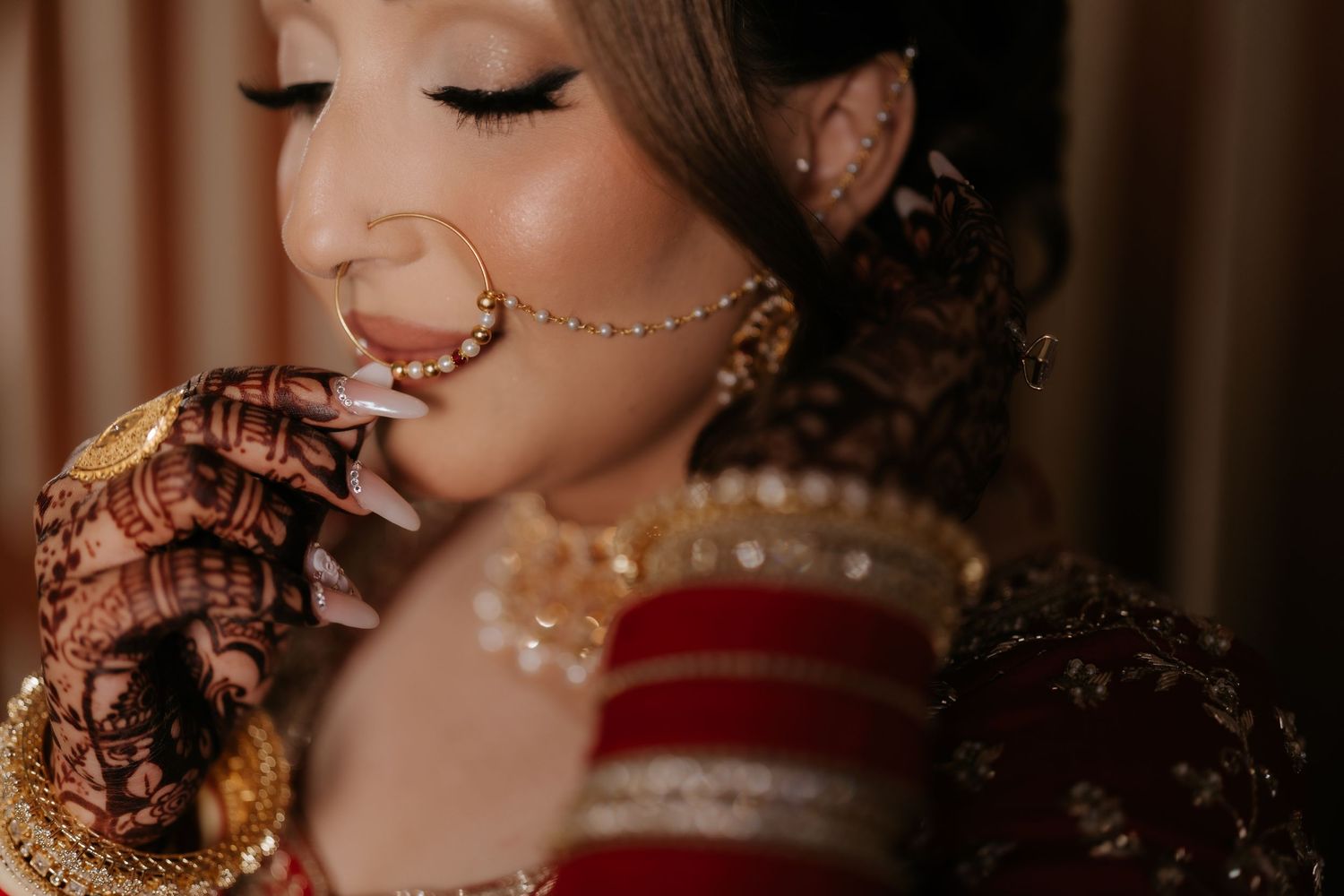 Indian bride in red lehenga with mehndi hands, gold jewelry, and maang tikka on her wedding day.