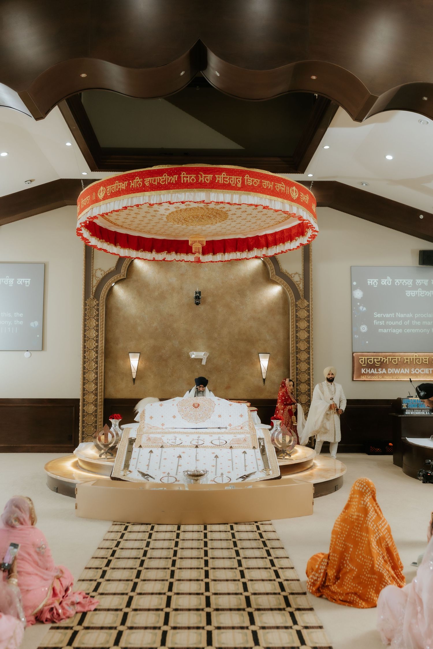 Sikh wedding ceremony at a Gurdwara with couple at the Palki Sahib beneath a decorative canopy.