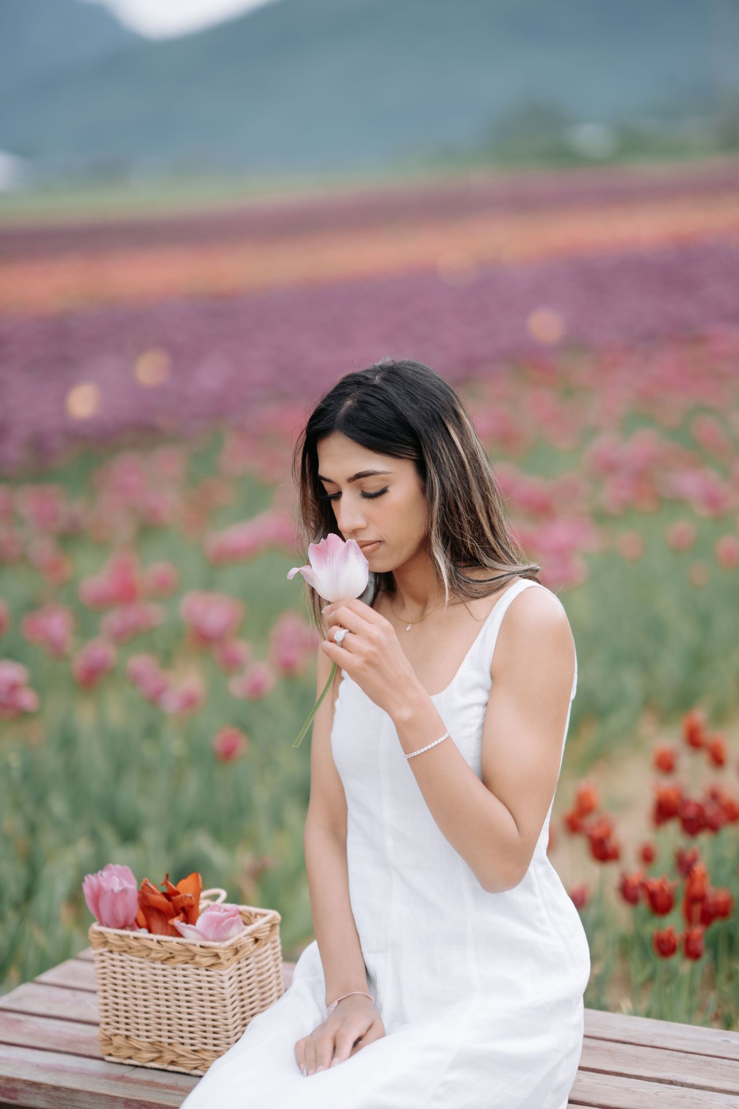 Woman in white dress enjoys tea and treats at outdoor table in blooming red poppy field on sunny day.