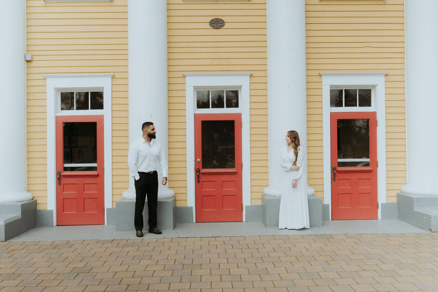 Architectural view of a yellow building with white columns and red doors creating a symmetrical facade.