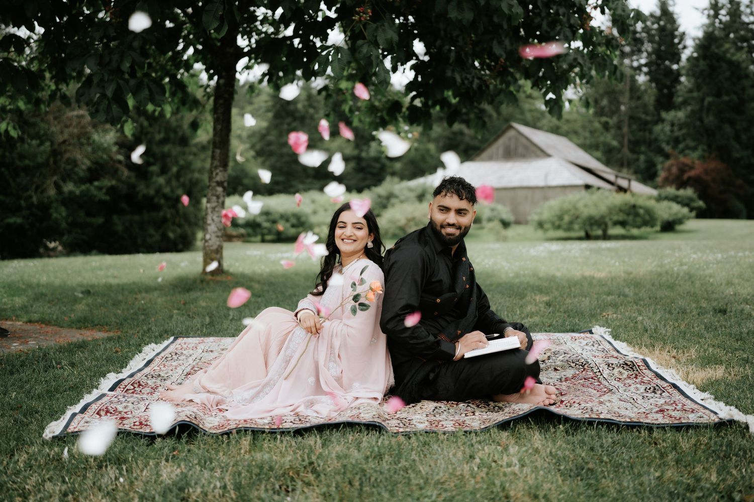 A romantic outdoor photoshoot in a park with scattered rose petals and a decorative blanket.
