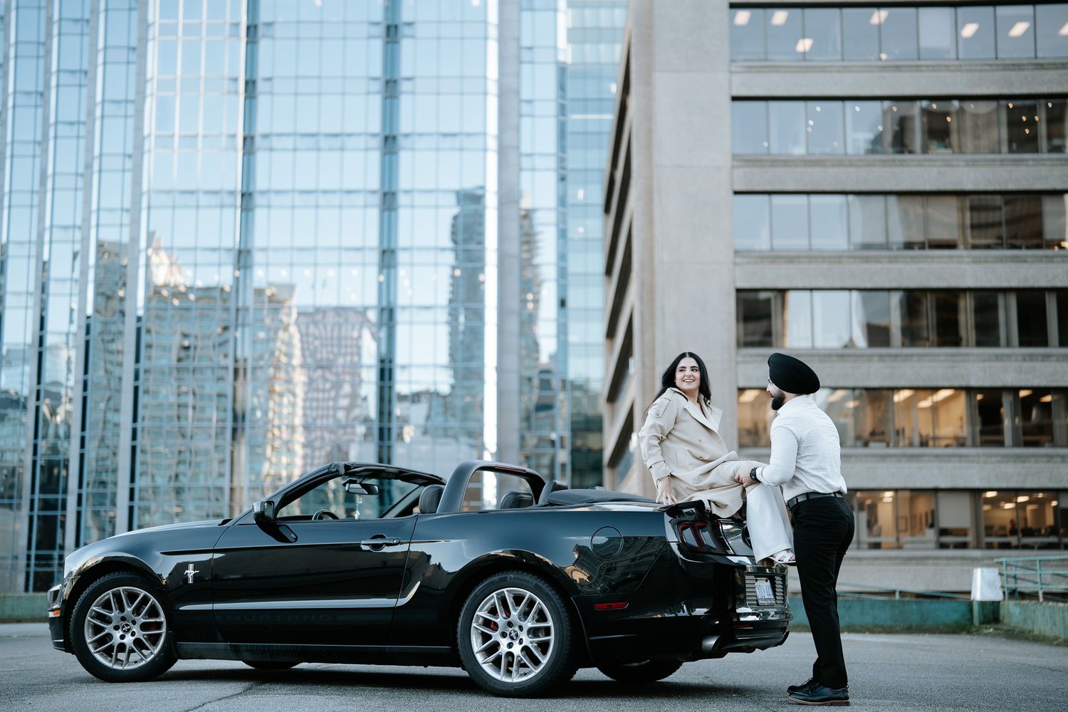 A sleek black luxury sports car parked in front of a modern glass building with reflective windows.