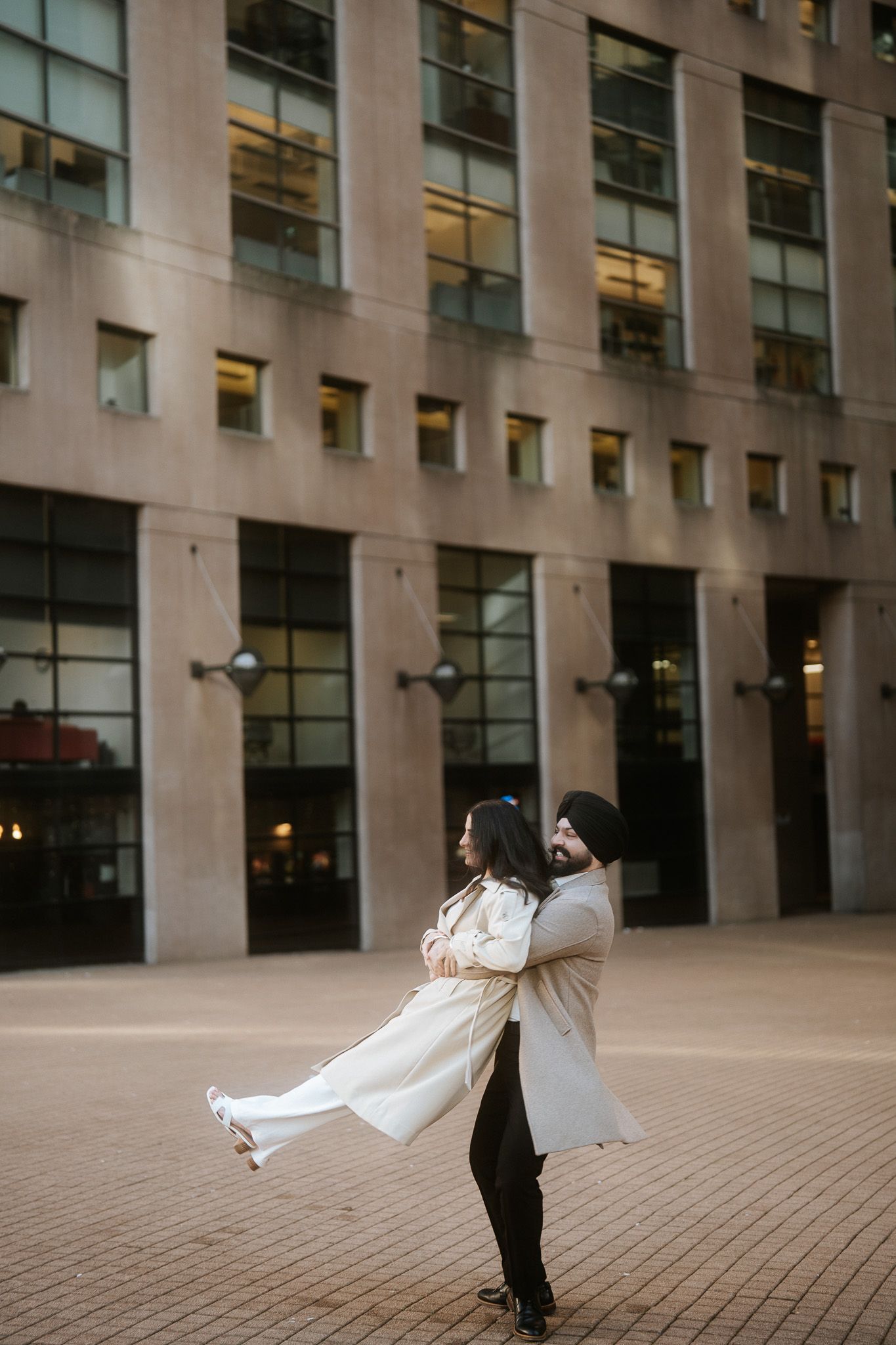 A romantic wedding couple dances and spins together on a paved courtyard outside a modern office building.