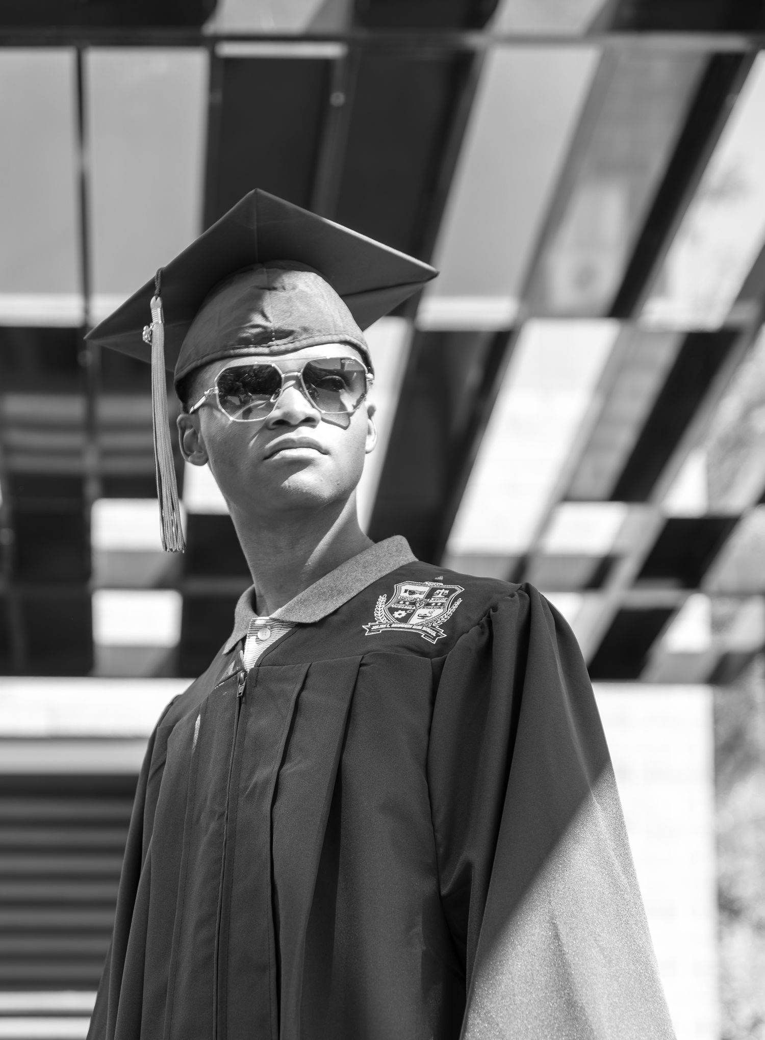Young man in graduation cap, gown, and sunglasses posing proudly in black and white photo.